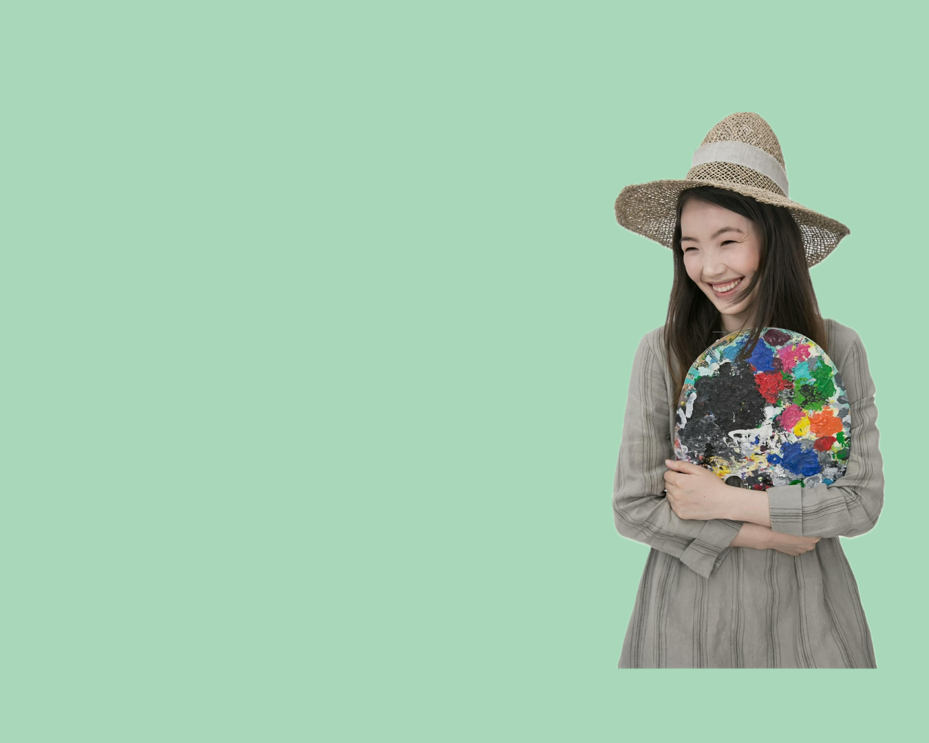 A smiling young woman wearing a wide-brimmed straw hat and a gray striped dress, holding a colorful artist's palette with various paint colors, standing against a light green background.