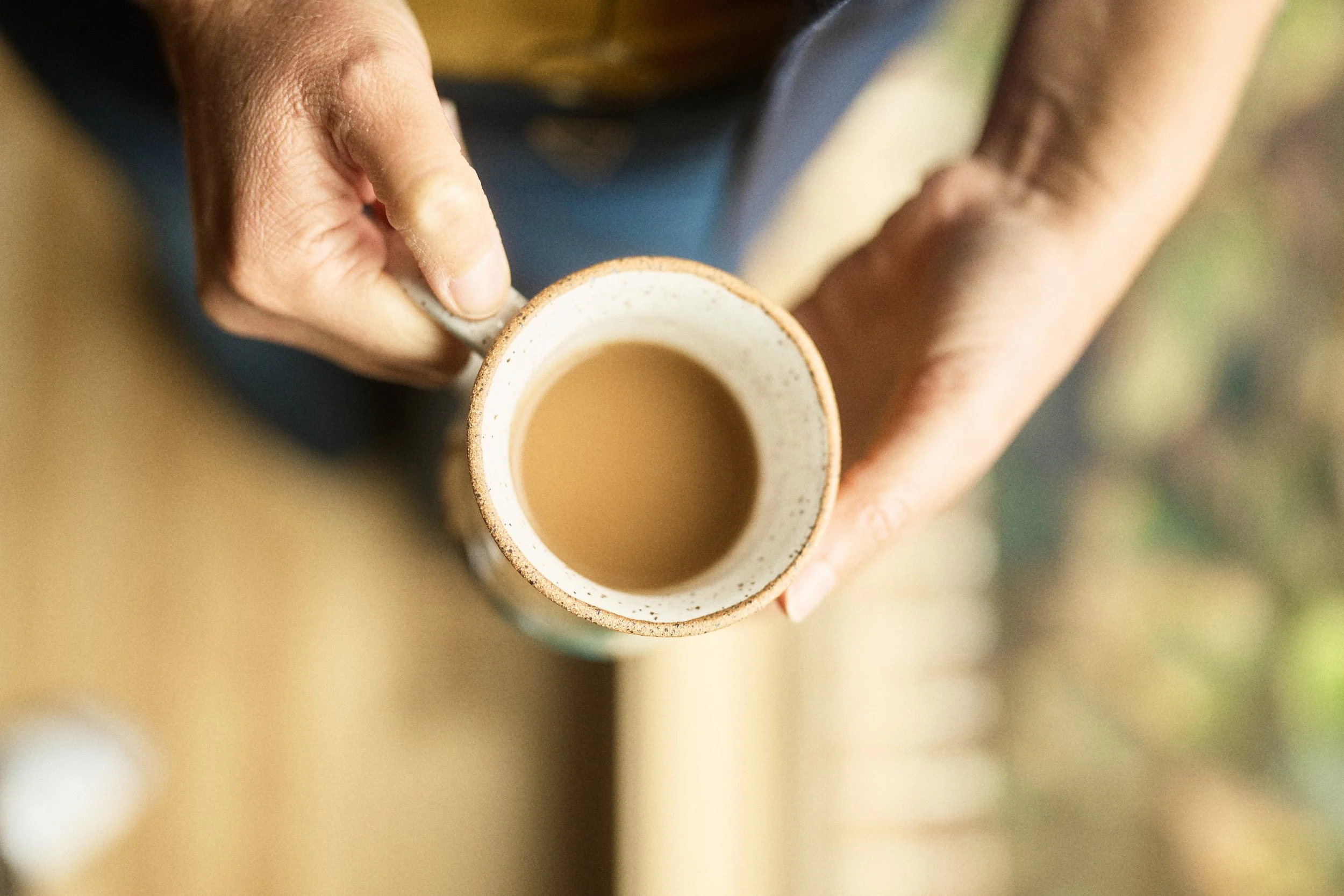 A person holds a ceramic mug filled with coffee or tea, viewed from above.