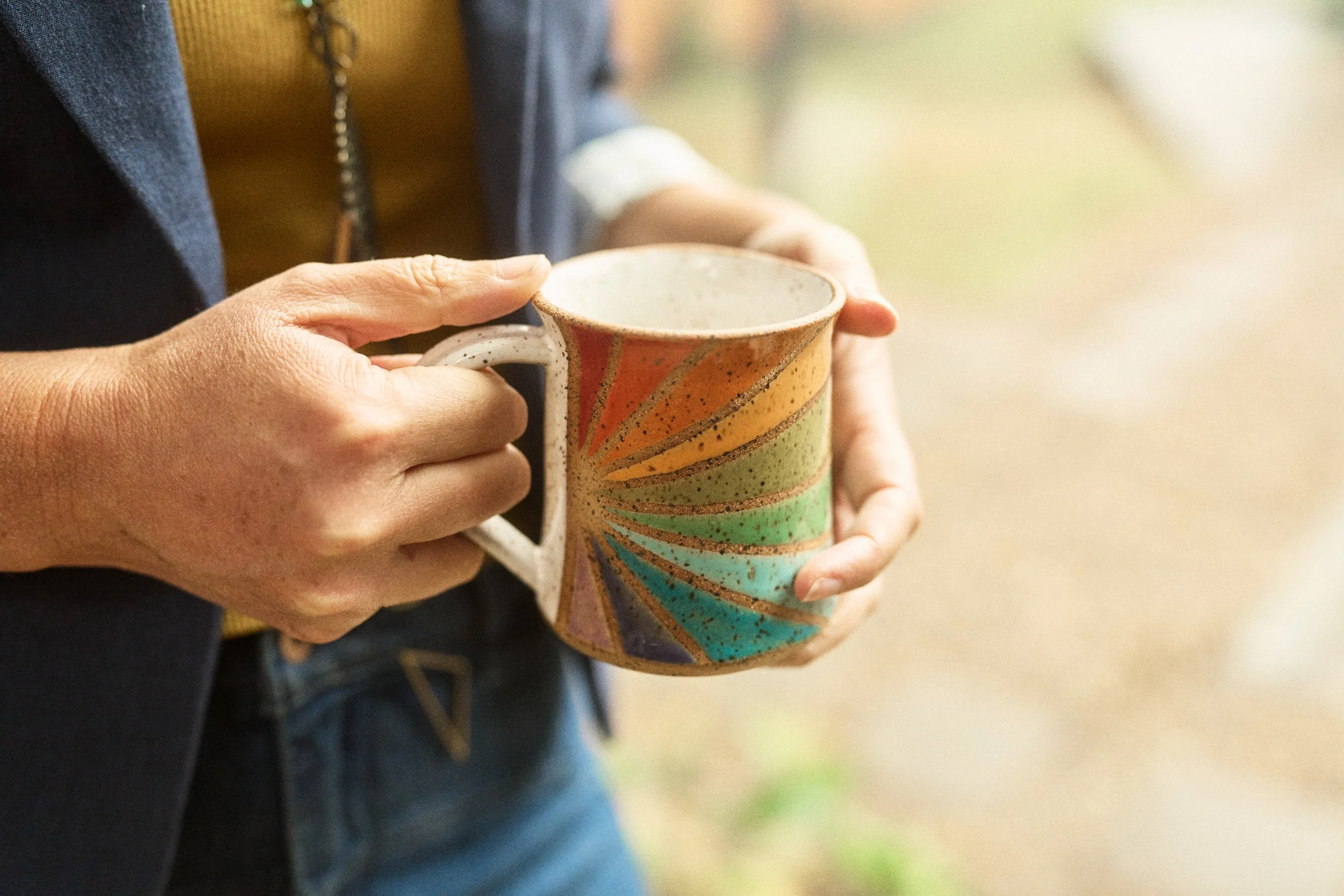 Person holding a colorful, handmade ceramic mug with a swirl design in orange, green, blue, purple, and yellow hues.