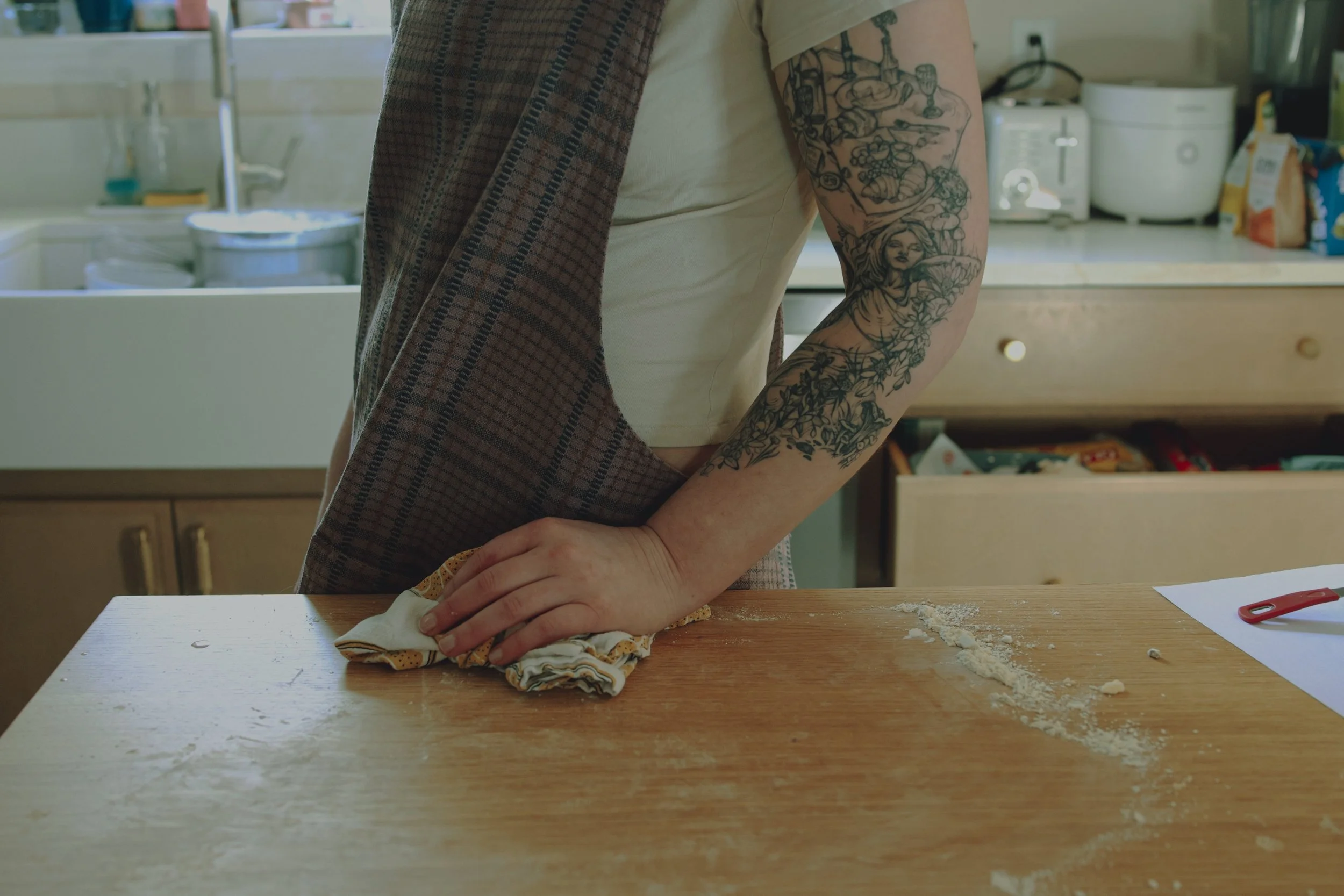 Person with tattoos on their right arm rolling out dough on a kitchen counter in Somerville, NJ