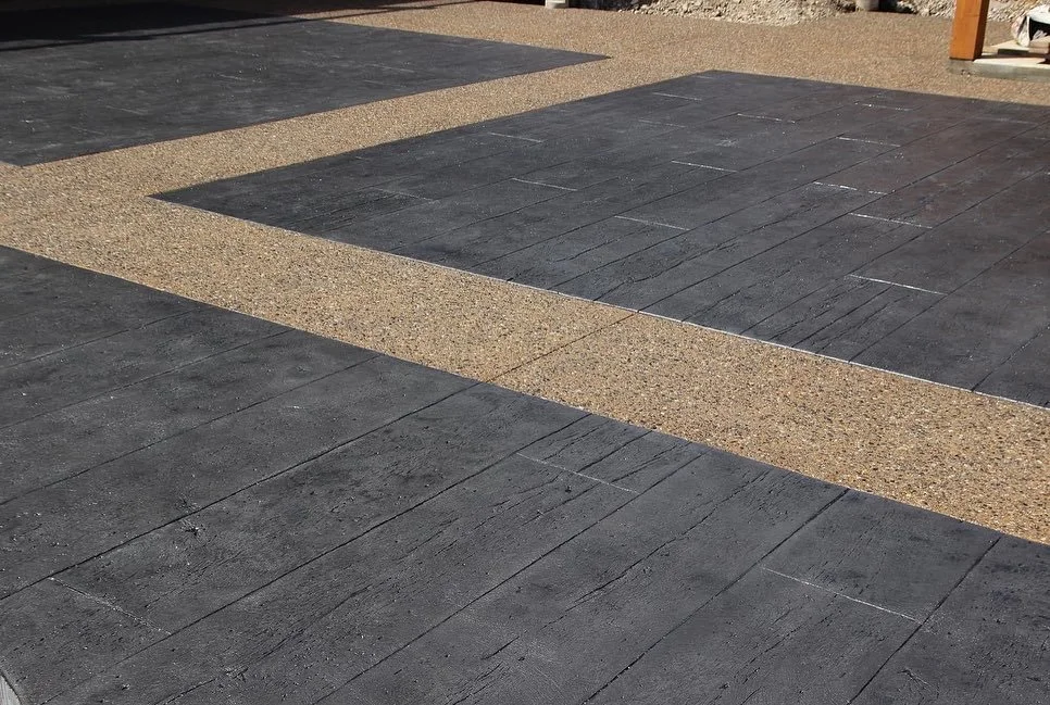 Close-up of a paved surface with alternating black and tan-colored tiles arranged in a geometric pattern.