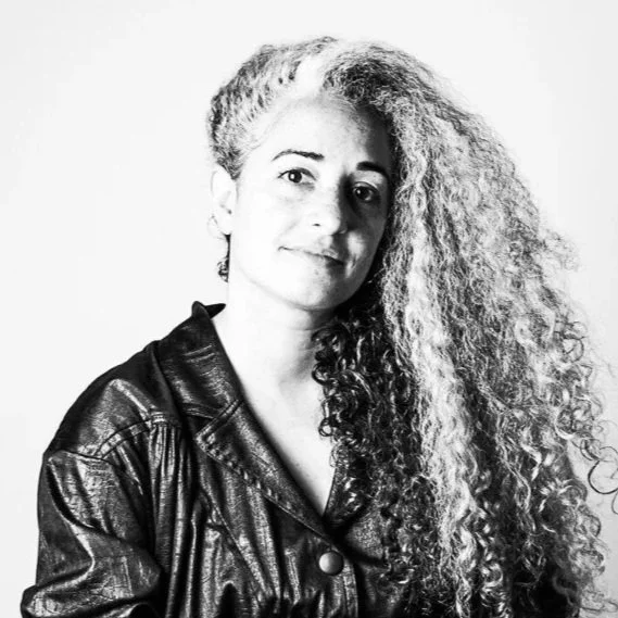 Black and white portrait of a woman with long, curly hair wearing a leather jacket.