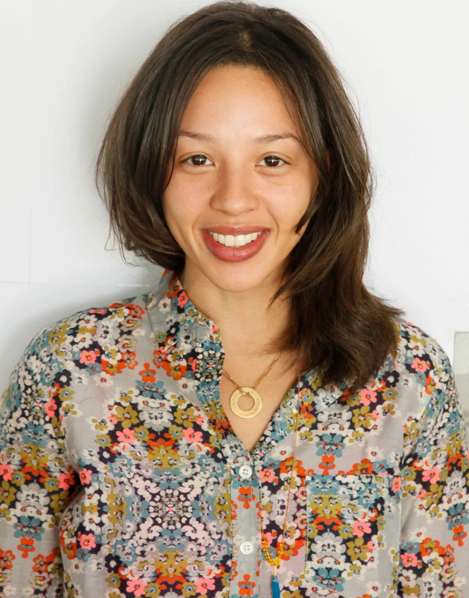 A woman with shoulder-length brown hair wearing a floral shirt and gold jewelry, smiling at the camera.