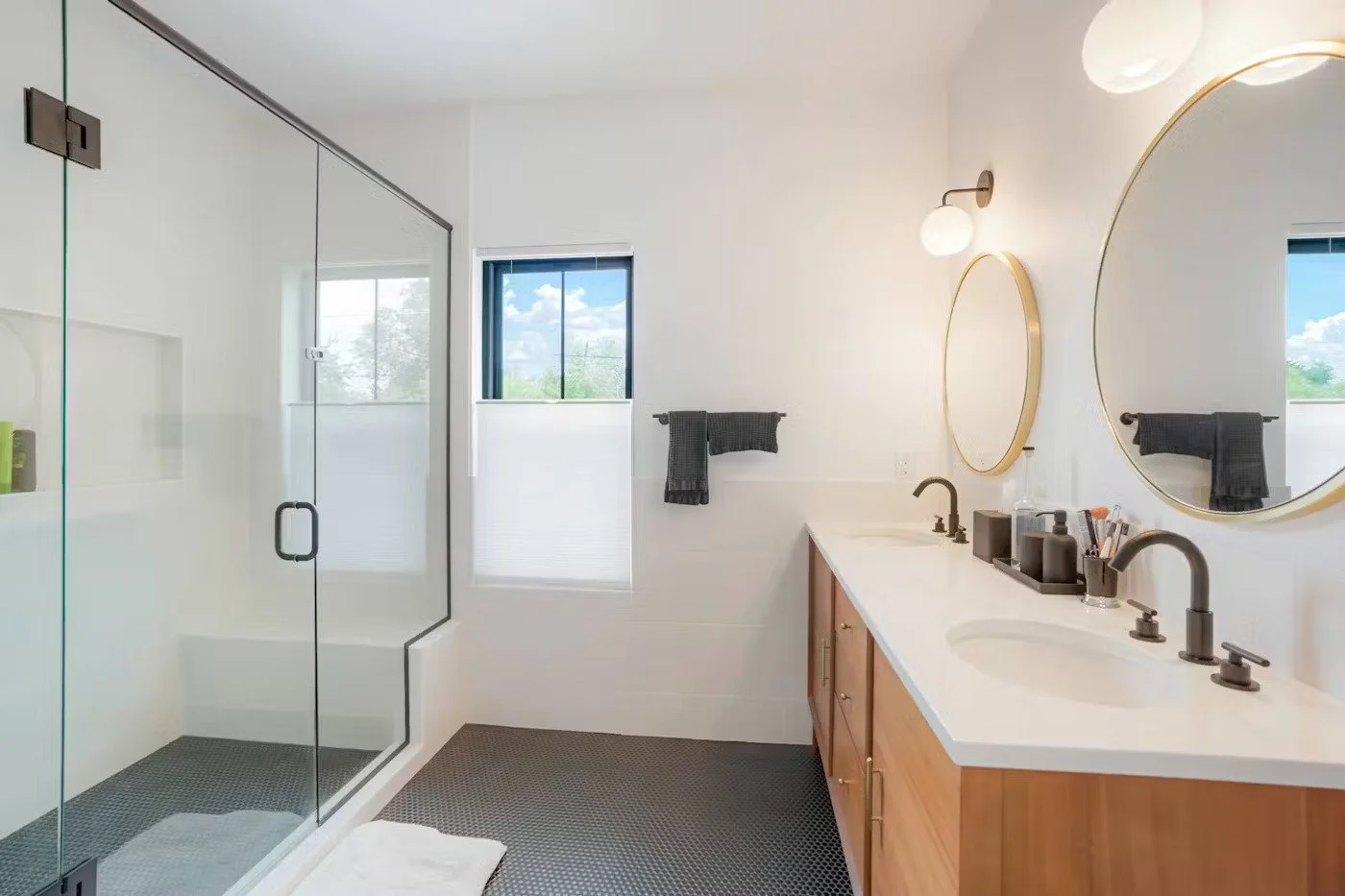 Modern bathroom with double vanity, round mirrors, black fixtures, and a glass-enclosed shower.