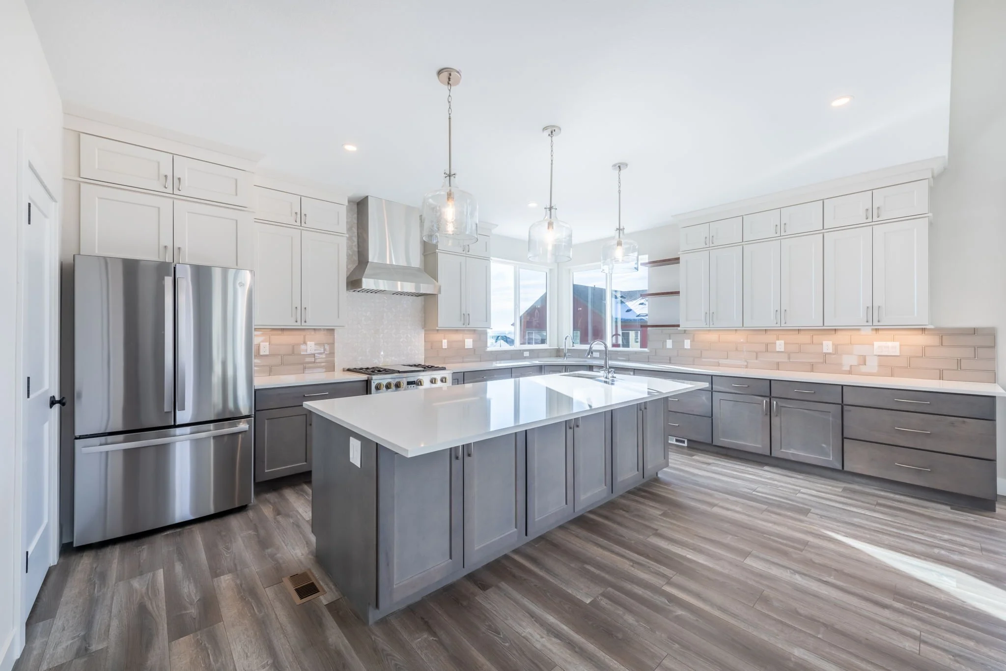 Modern kitchen with white upper cabinets, gray lower cabinets, stainless steel appliances, and a large island with a white countertop.