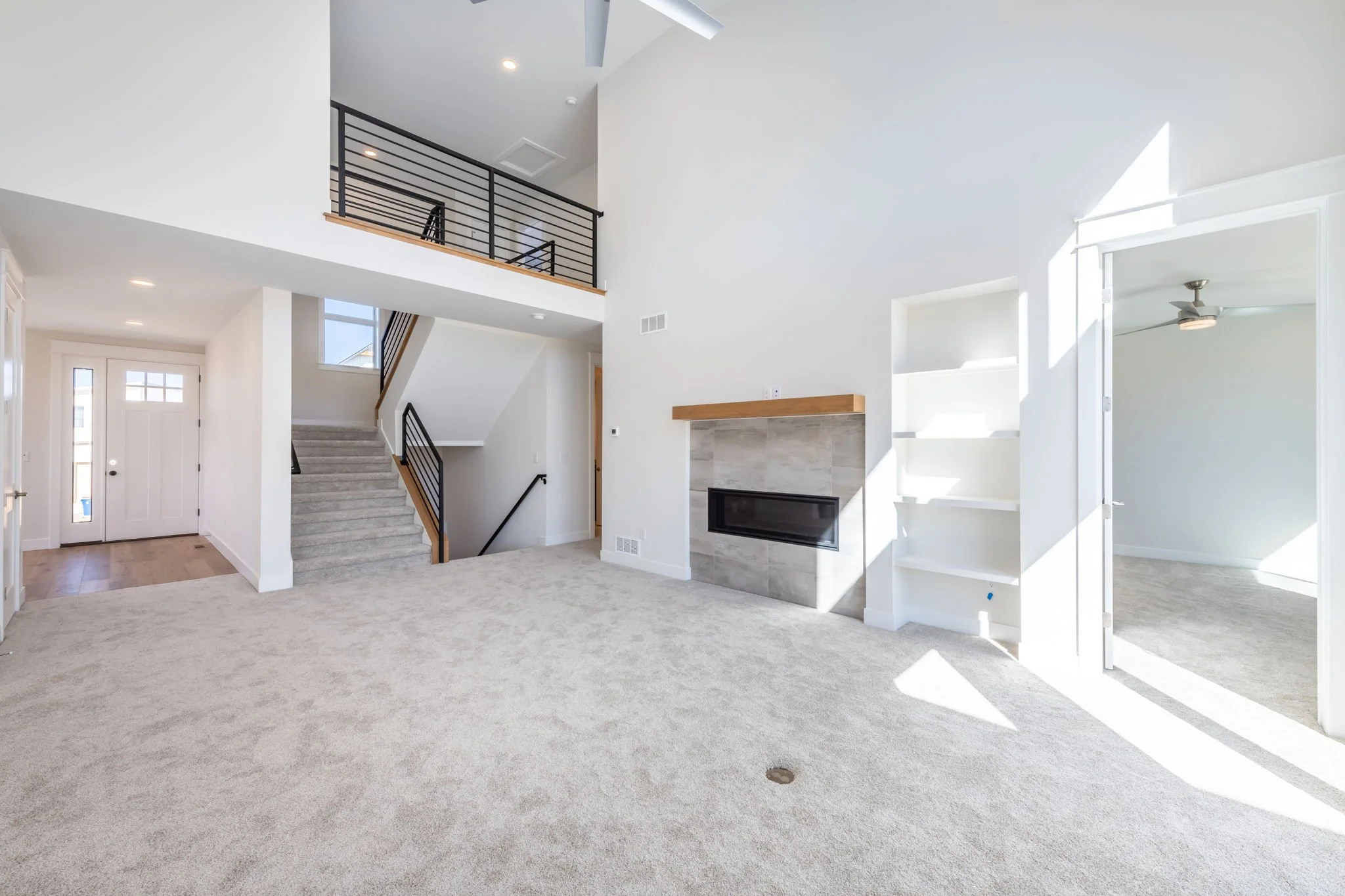 Empty living room with fireplace, built-in shelves, carpeted floor, and staircase leading upstairs, with bright natural light.