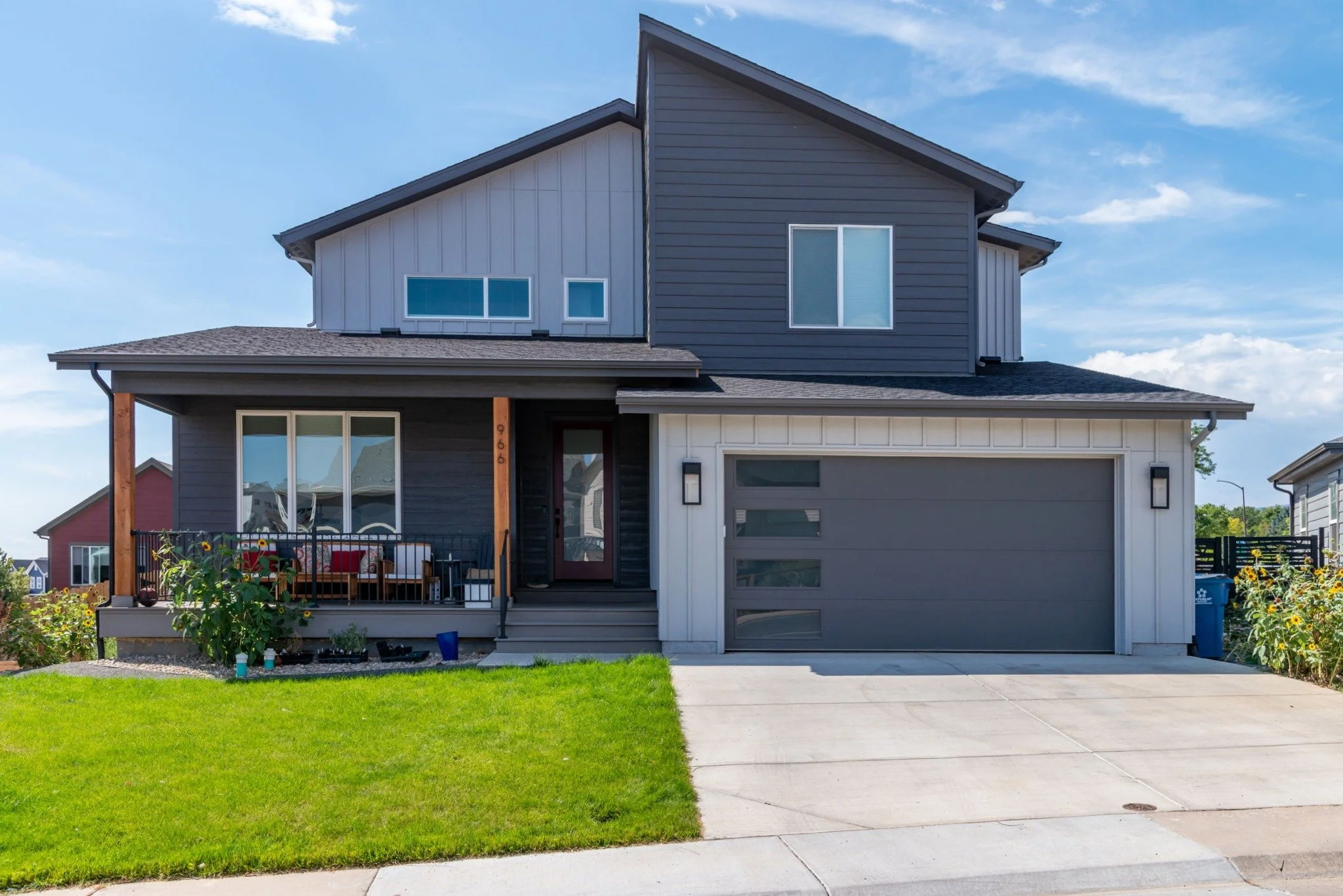 Modern two-story Marshall fire rebuild house with gray and white exterior, small front porch with seating, and a two-car garage, under a blue sky. Louisville, CO.
