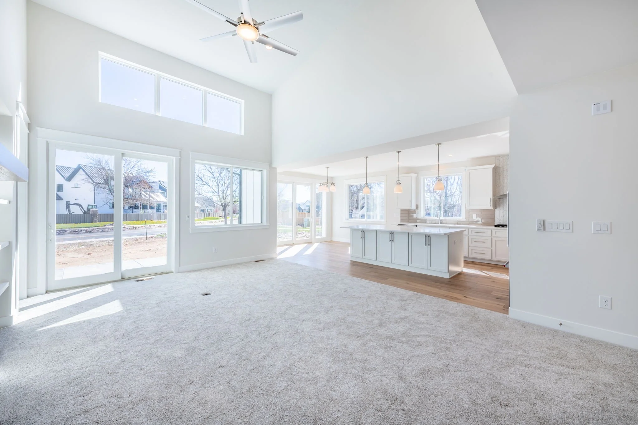 Bright open-concept living space with large windows, white walls, and a kitchen area featuring a central island and pendant lighting.