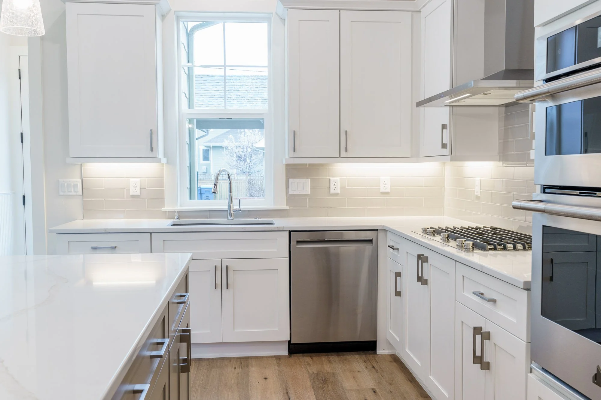 Modern kitchen with white cabinets, a window above the sink, stainless steel appliances, and wood flooring.