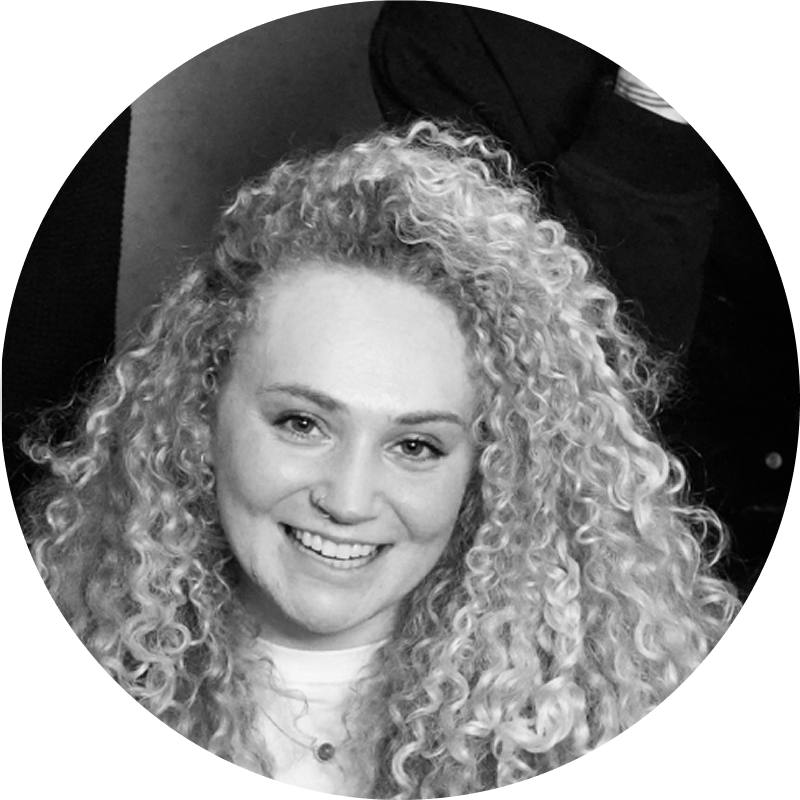 Close-up of a young woman with curly hair smiling at the camera in black and white.