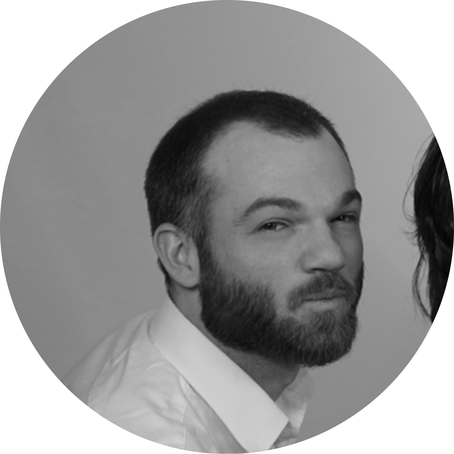 Black and white portrait of a man with short hair and a full beard, wearing a light shirt, looking slightly to the side with a neutral expression.