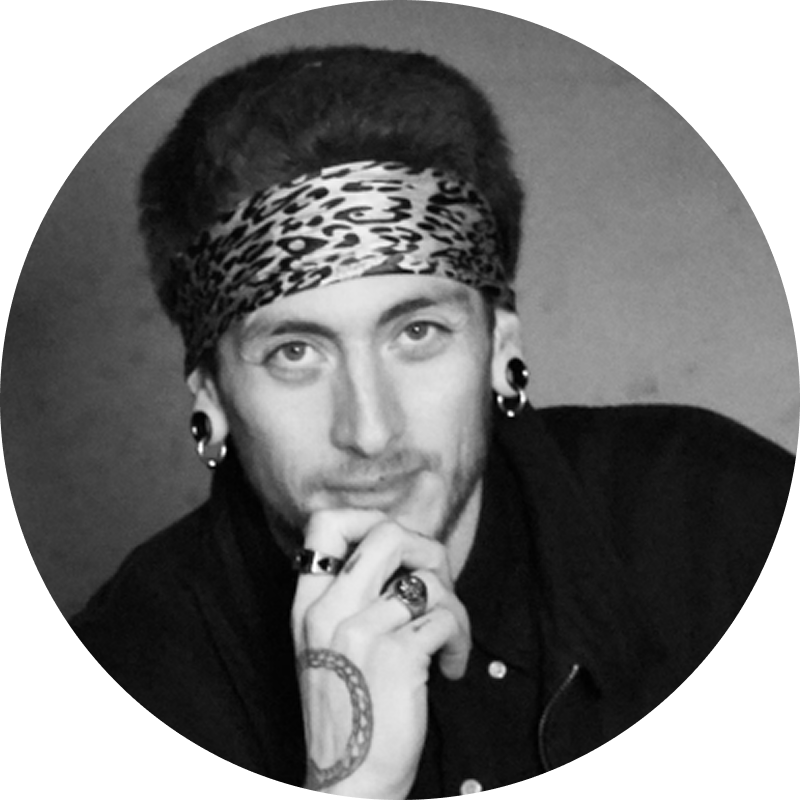 Black and white portrait of a man with earrings, rings, and a headband, resting his chin on his hand and looking at the camera.