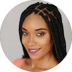 A woman with braided hair and purple lipstick, smiling at the camera.