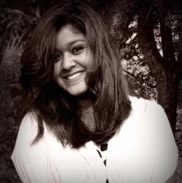A smiling young woman outdoors with trees in the background, black and white photo.