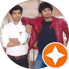 Two young men standing side by side, one in a white shirt and the other in a red jacket, smiling at the camera.