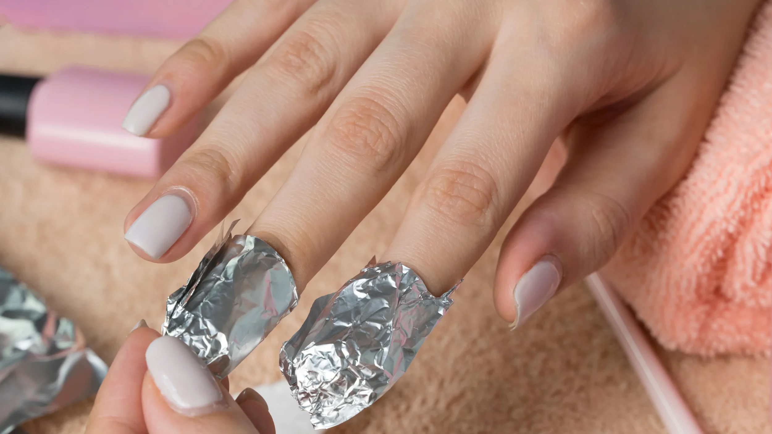 Close-up of a person applying white nail polish, with foil wrapped around their fingers for a manicure process.