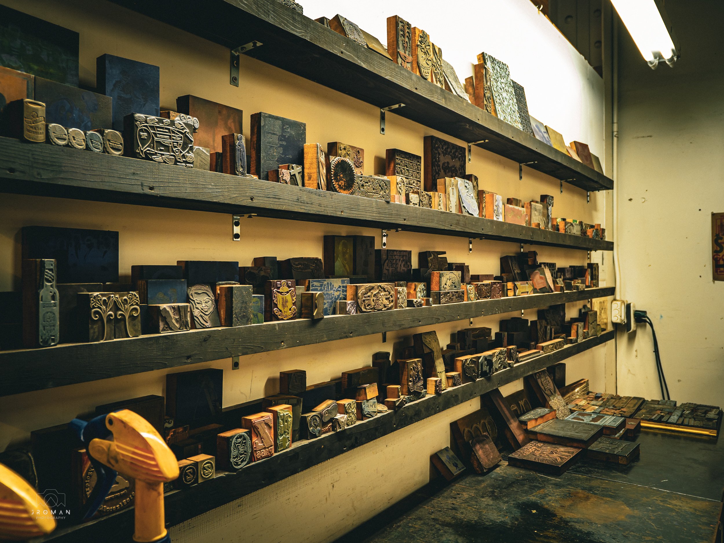 Wall of shelves displaying various carved rubber stamps in a workshop.