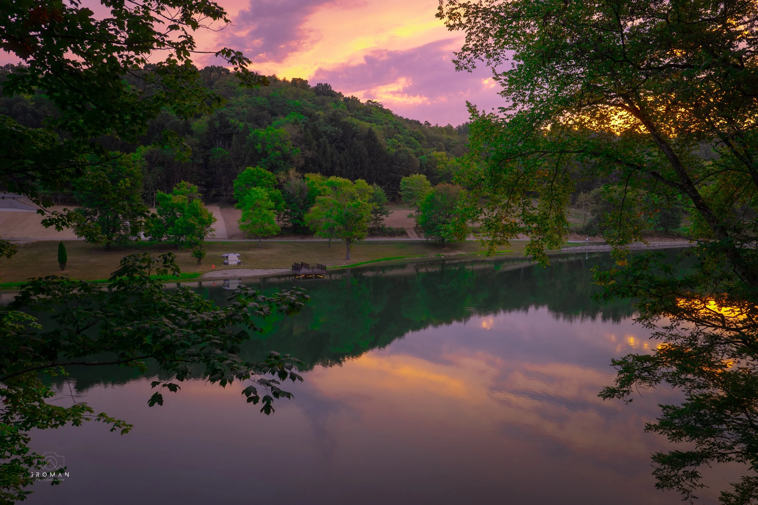 Sunset over a calm river reflecting colorful sky and surrounding green trees.