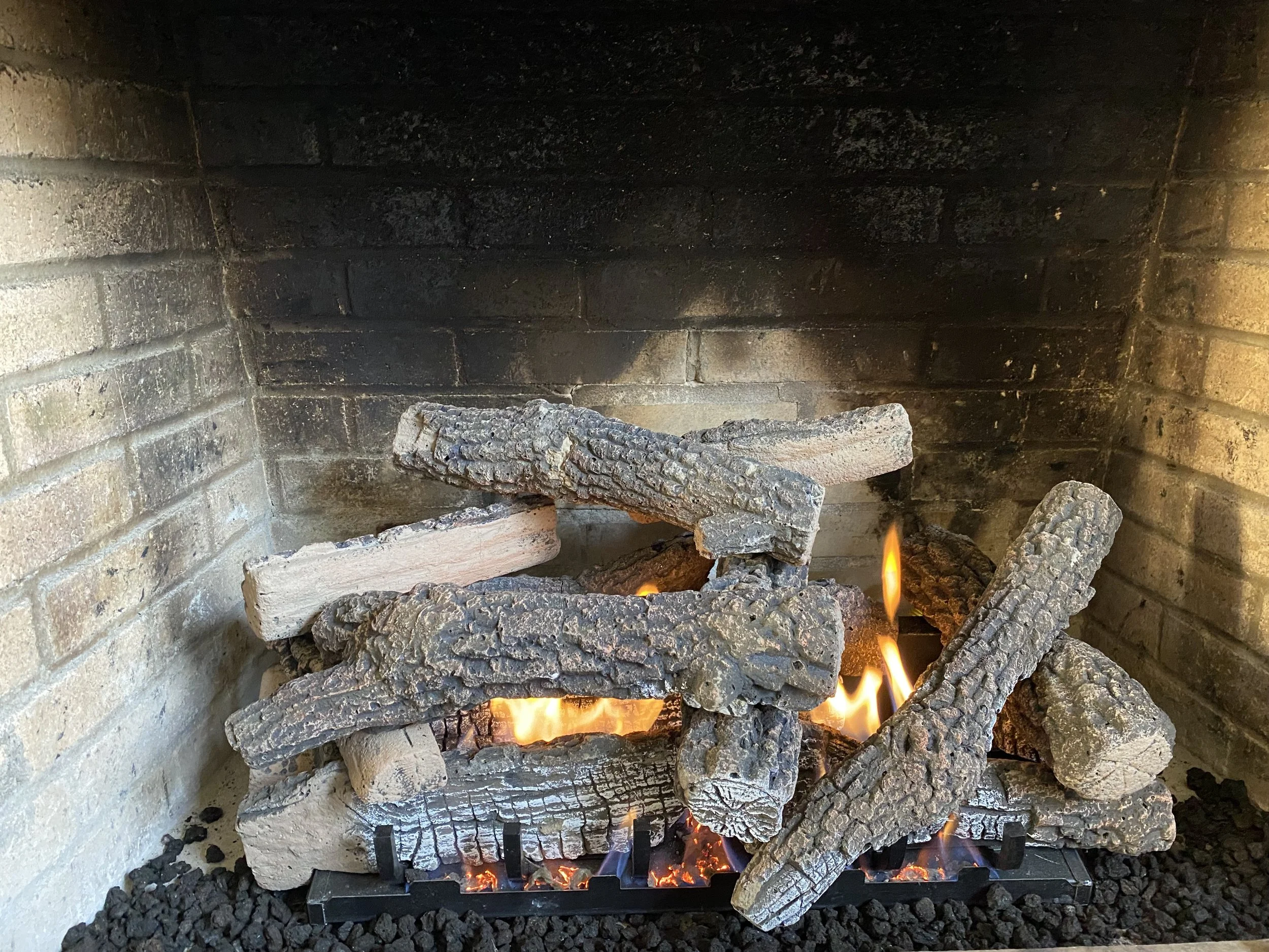 A fireplace with burning logs and flames, surrounded by a brick interior.