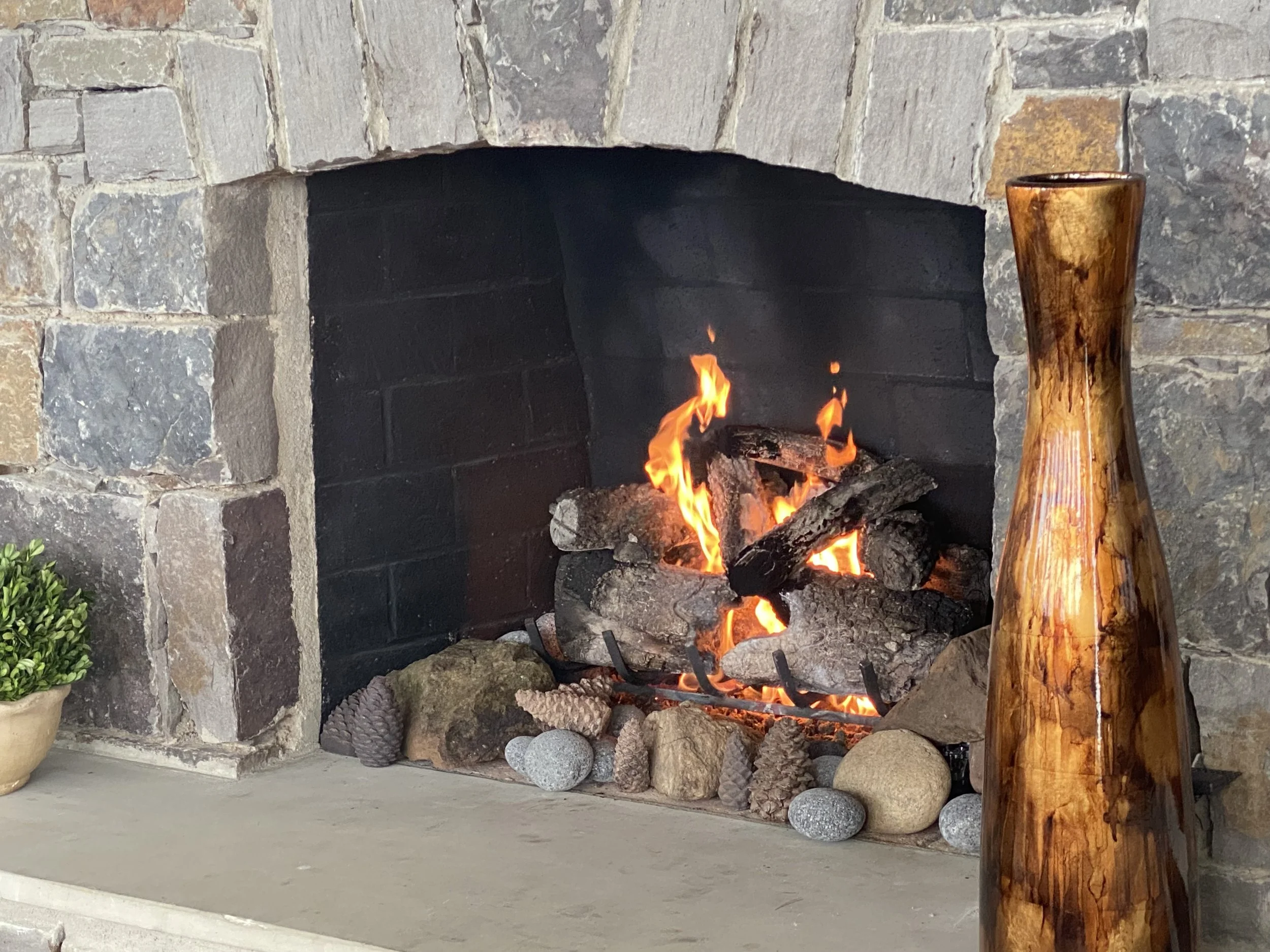 A fireplace with a fire burning inside, surrounded by stones and rocks, with a wooden log placed nearby.