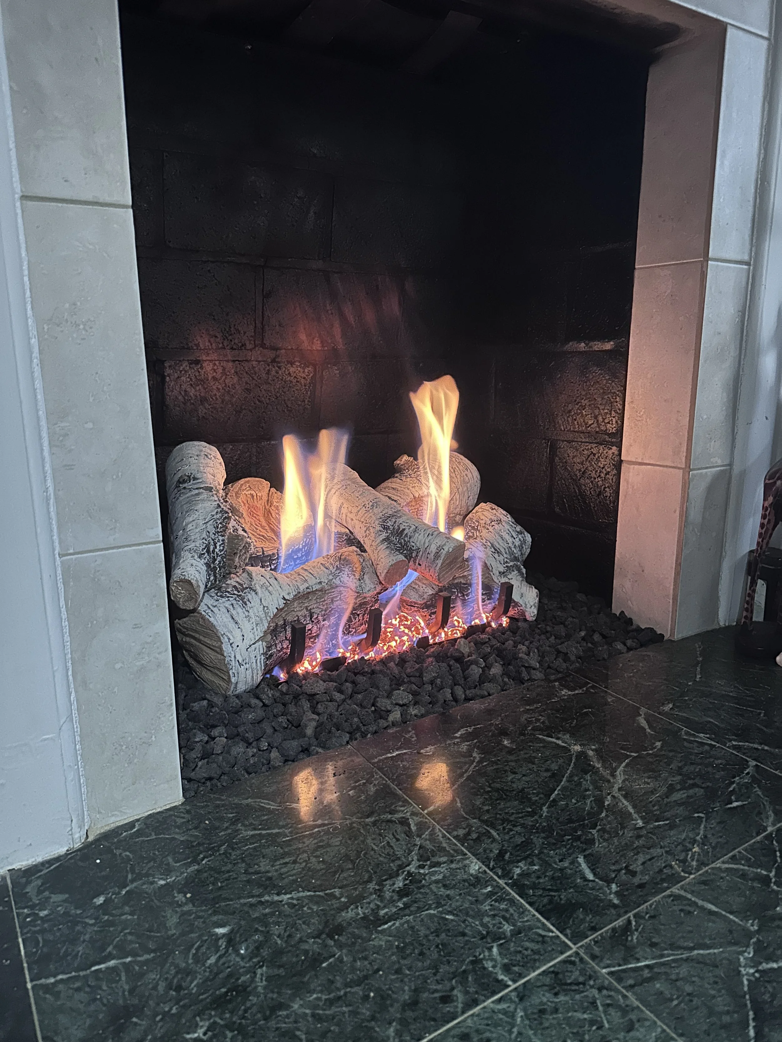 Fireplace with glowing logs and flames, surrounded by black and white tile and marble flooring.