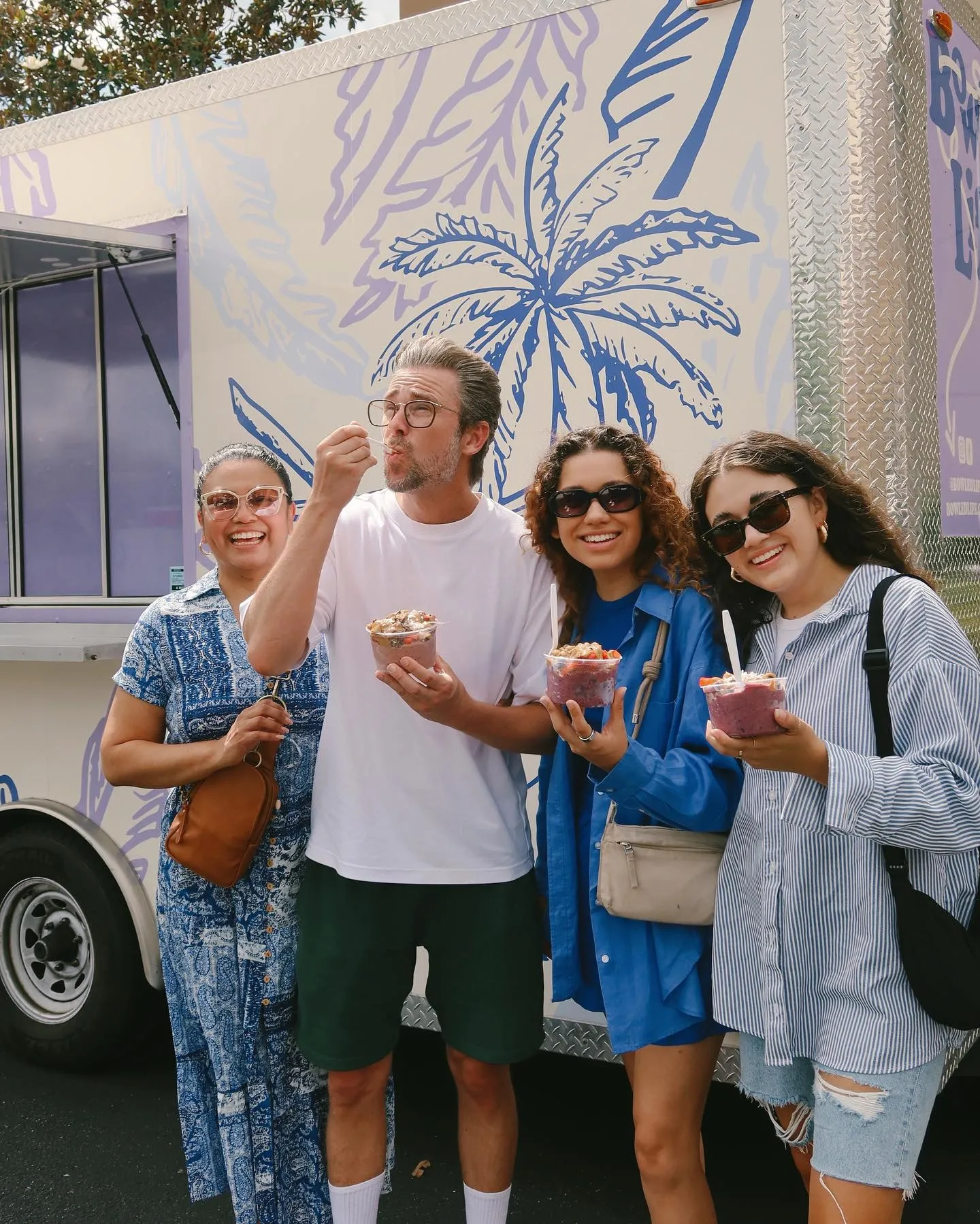 Four people enjoying ice cream outside of an ice cream truck with a palm tree illustration on it. They are smiling and wearing casual clothing and sunglasses.