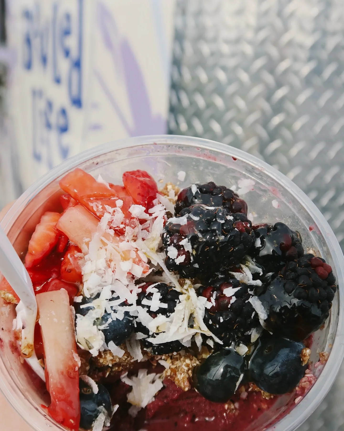 Close-up of a cup of frozen yogurt topped with strawberries, blackberries, blueberries, coconut flakes, and granola, with a spoon.