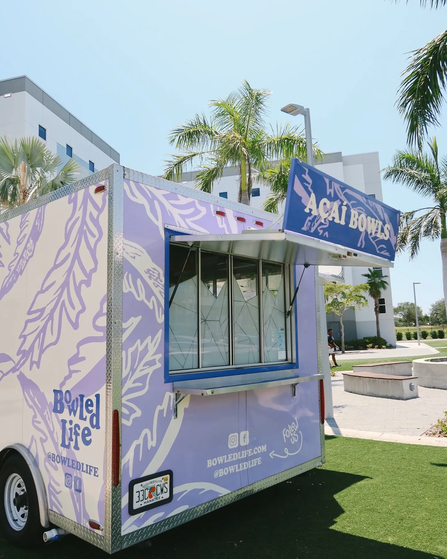 Purple food truck named 'Açaí Bowls' with palm trees and a modern building in the background.