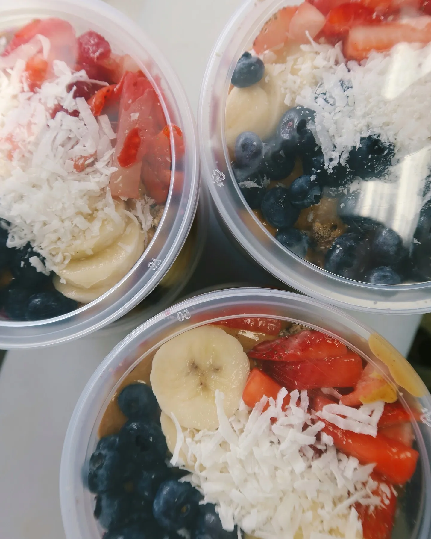 Three cups of fruit salad with blueberries, sliced bananas, shredded coconut, and chopped strawberries.