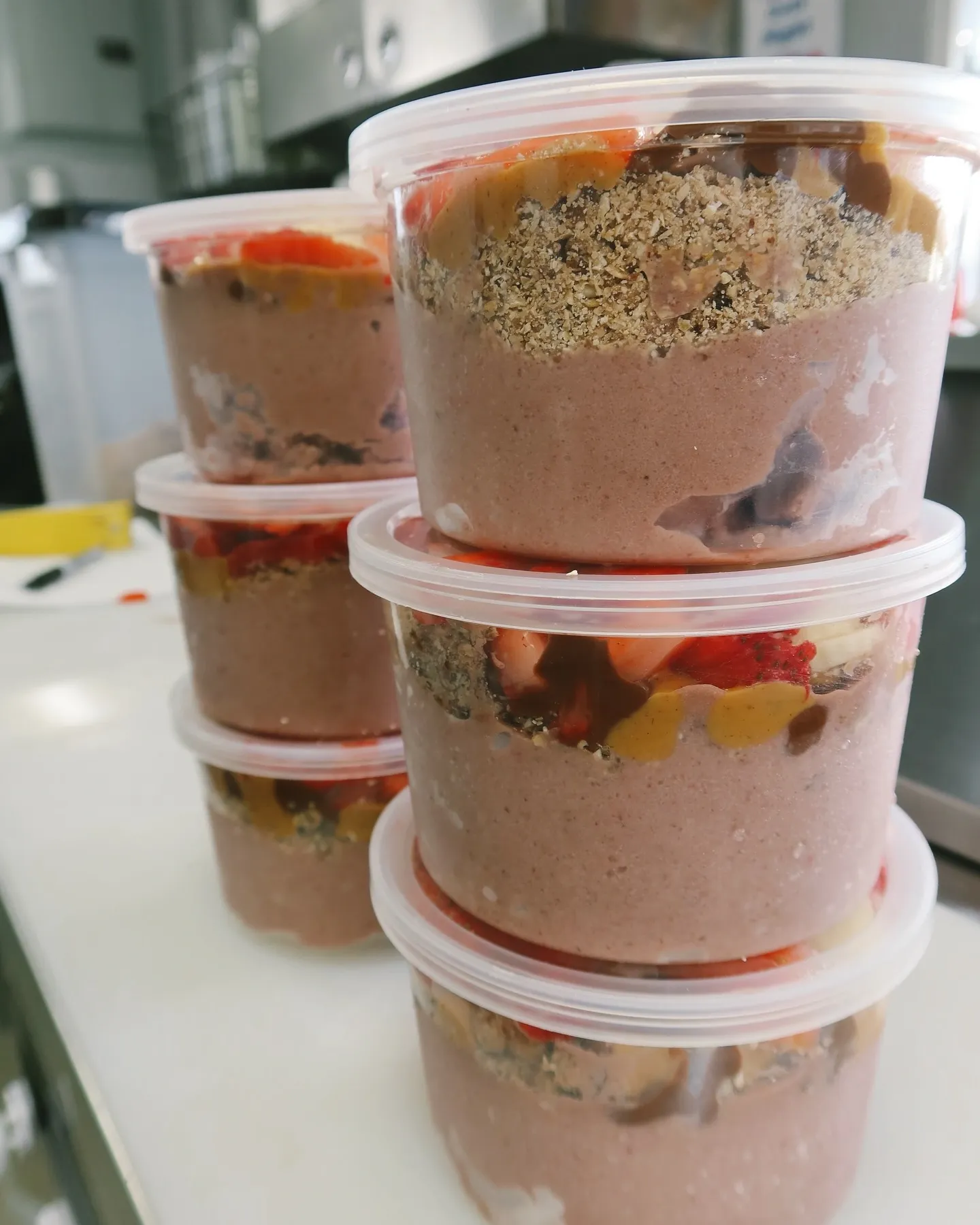 Stack of clear plastic containers filled with a layered dessert, possibly pudding or mousse, topped with chopped nuts and fruit pieces.