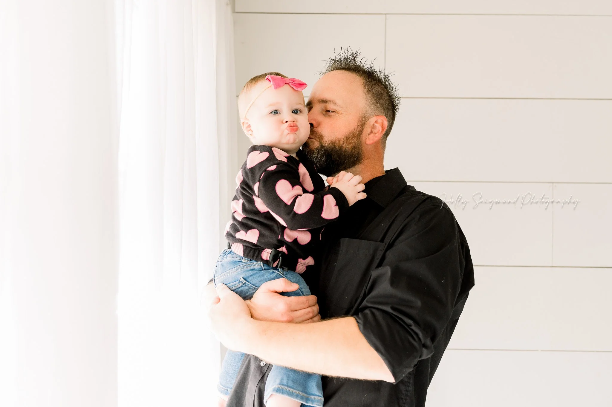 Dad kissing baby girl during a first birthday session in a natural light studio in Central Texas