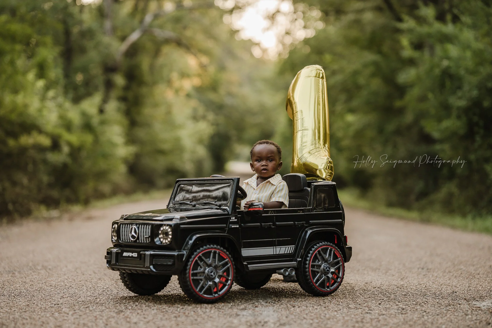 Boy's first birthday photo in his toy car with a 1 balloon in Central Texas