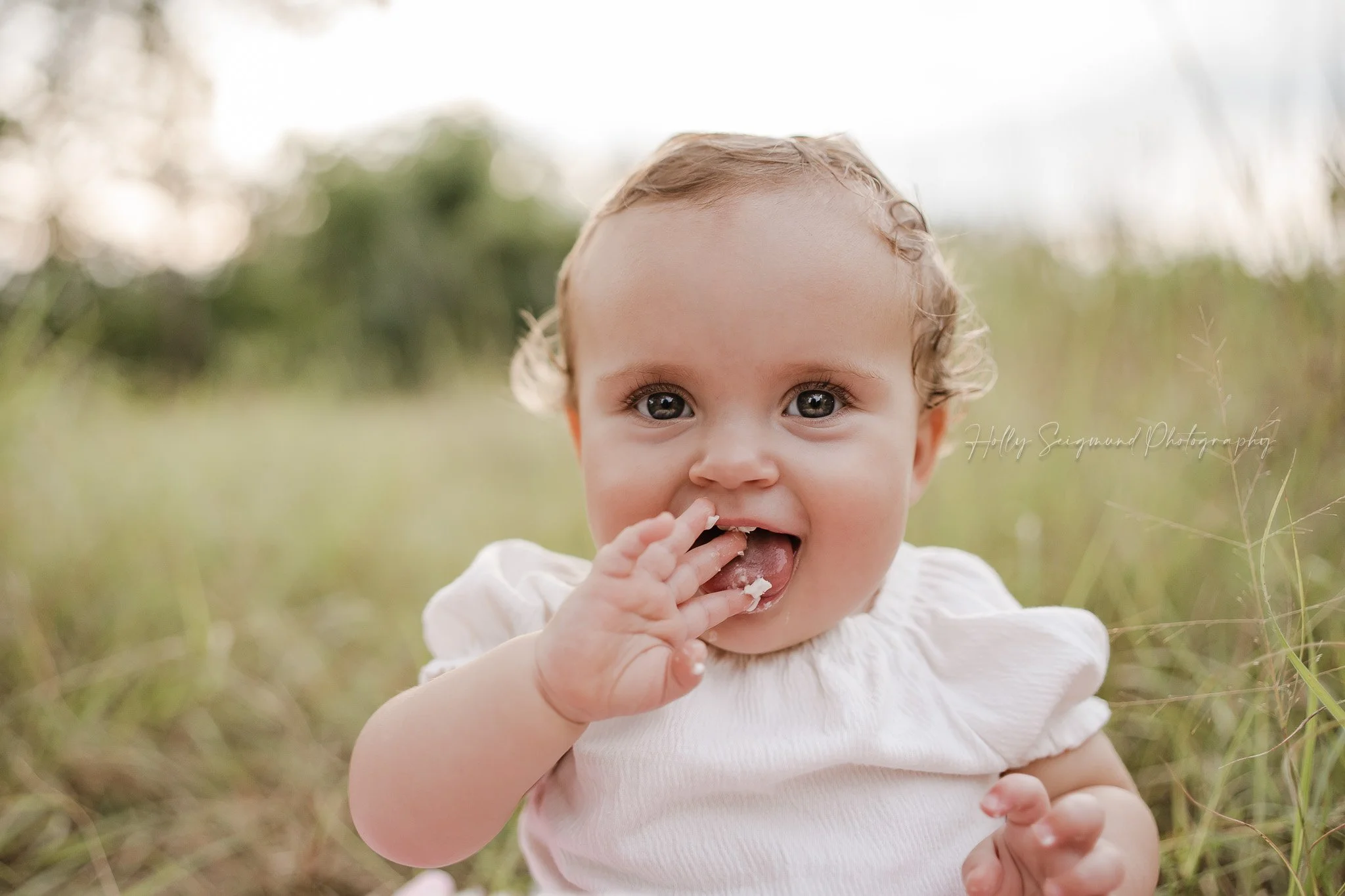 One year old girl eating icing off of fingers in the grass near Elgin, Texas