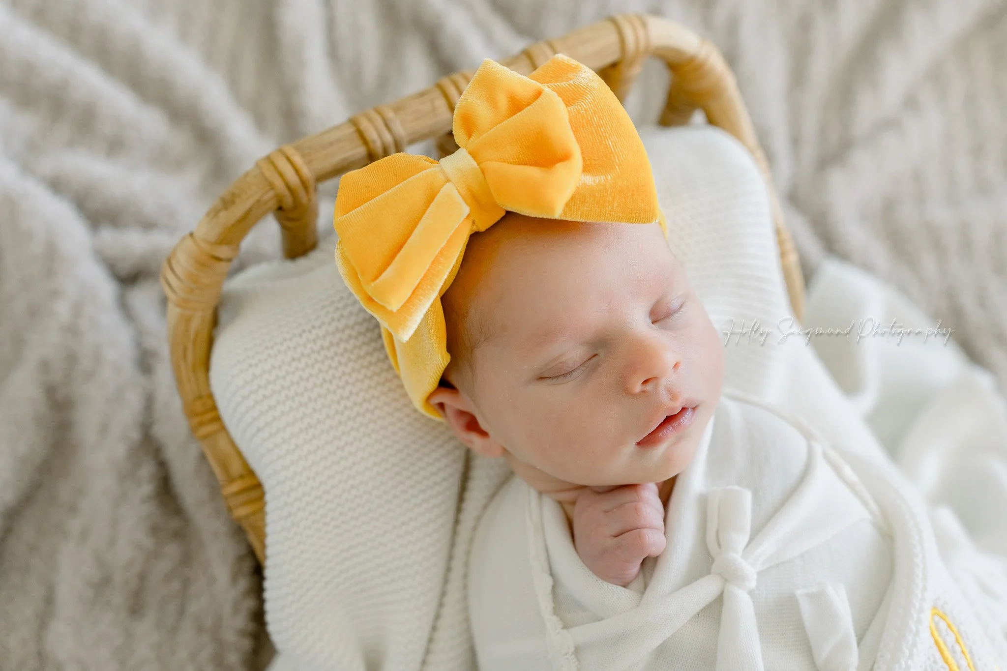 In-home newborn photos in Central Texas with a baby girl with a yellow bow in a wooden baby bed