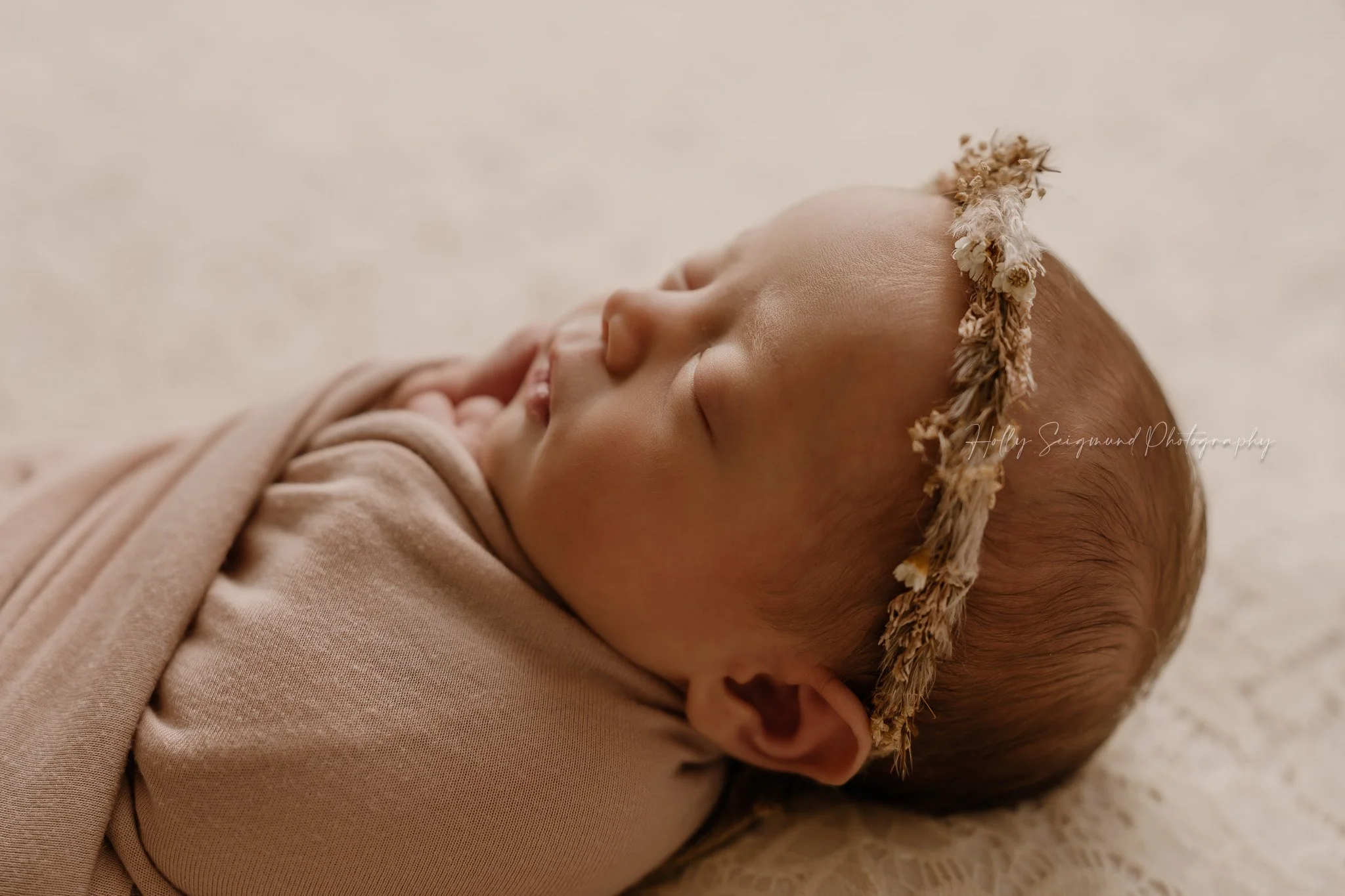 Newborn with a floral crown wrapped in pink on a lace background in a newborn photo studio in Lee County Texas
