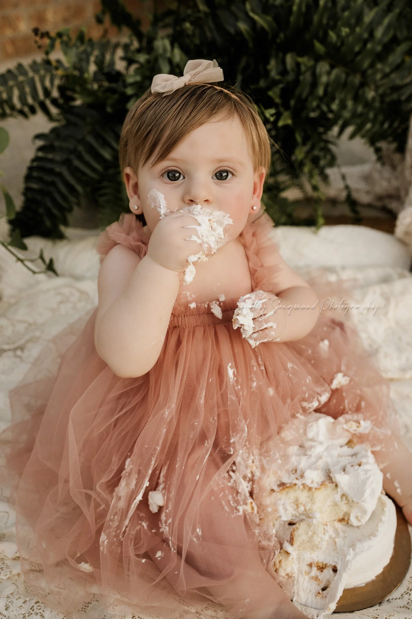 One-year-old celebrating her first birthday with a cake smash in a boho studio setup