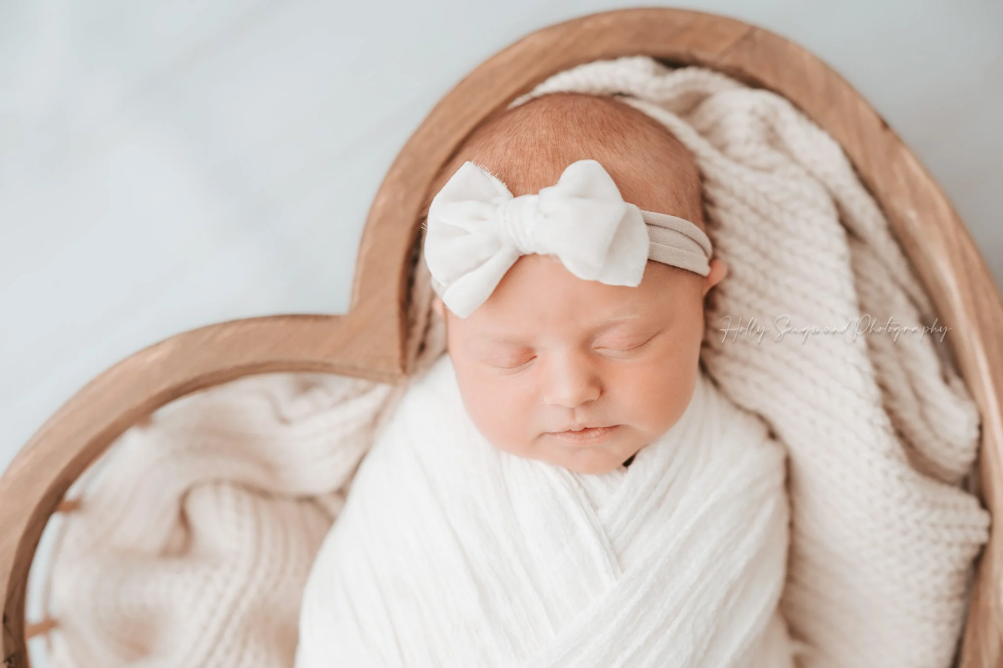 Central Texas newborn girl with white bow in wooden heart bowl on white floor