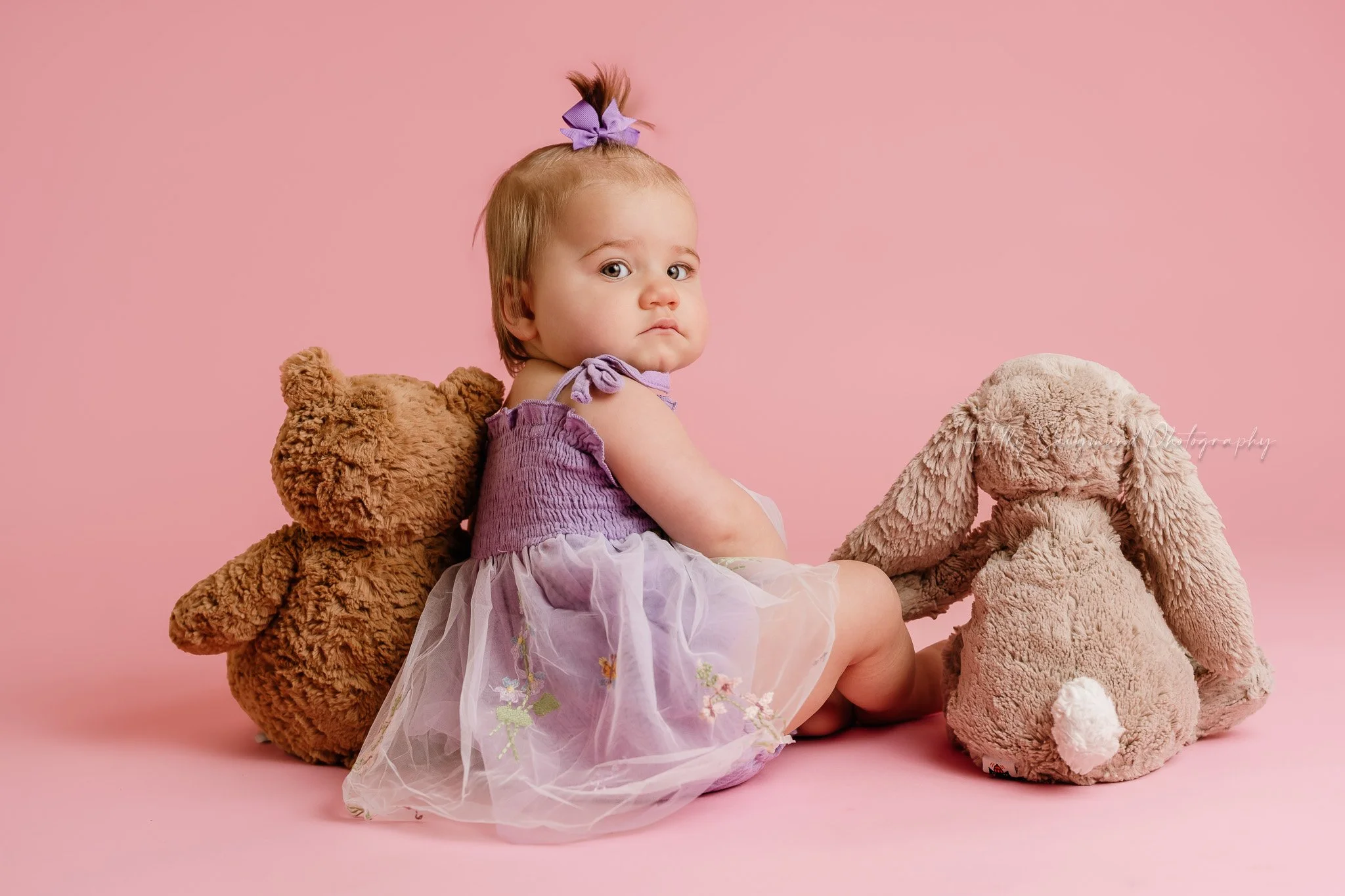 Girls first birthday photos with her stuffed animals in a studio with lights on pink paper in Central Texas