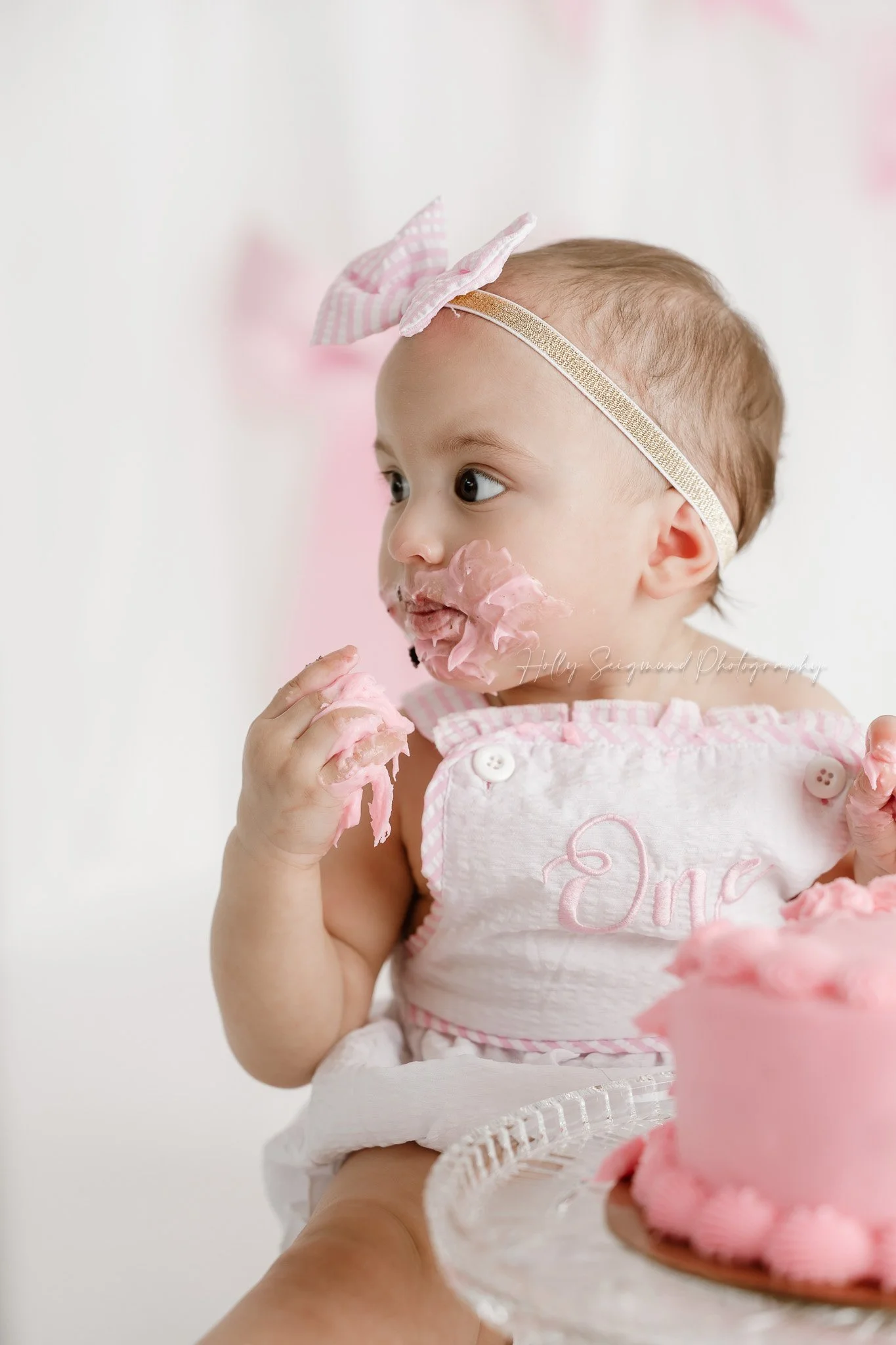 Little girls first birthday smash cake session with pink bows in a flash photography studio in Central Texas