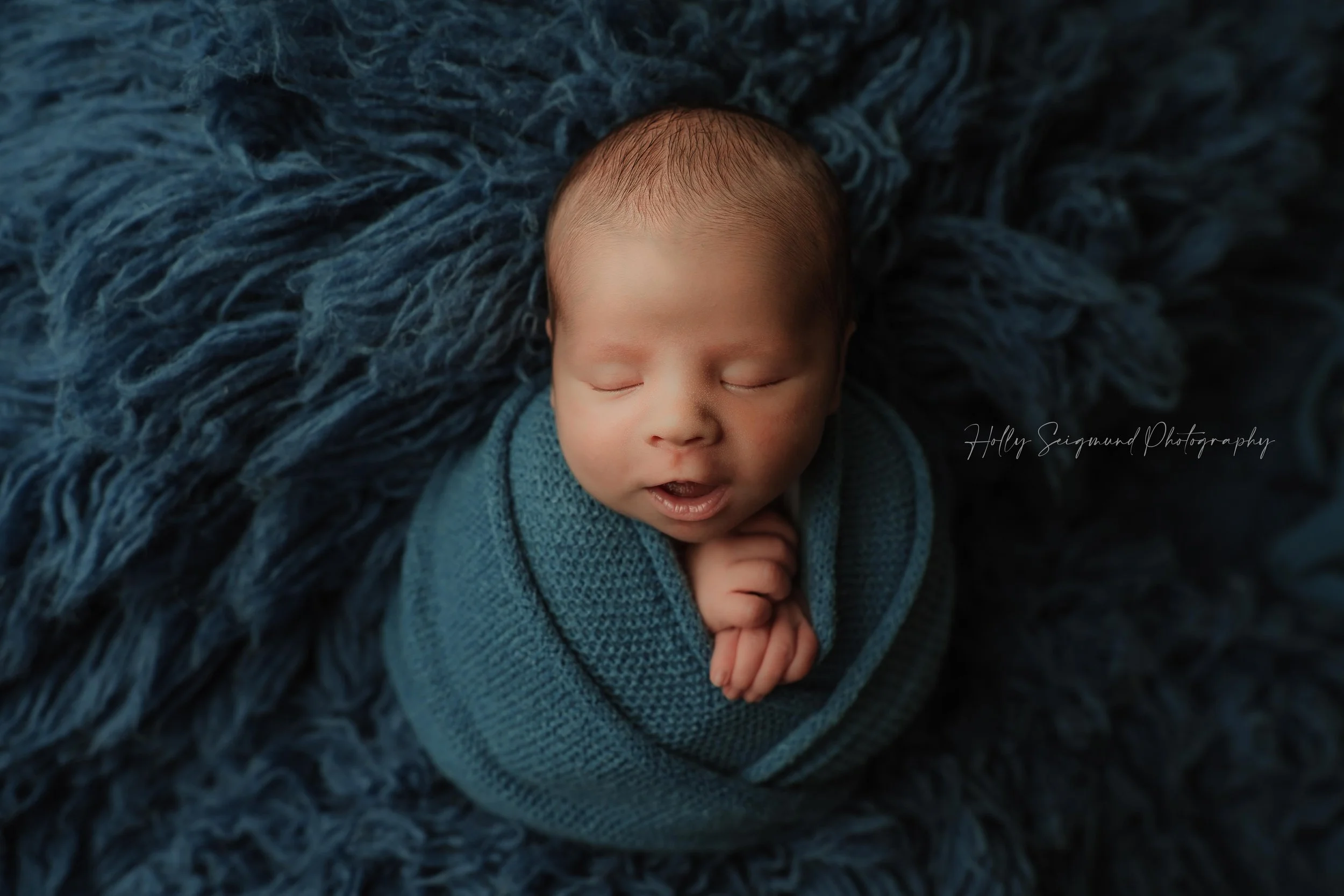 Newborn baby boy on a Navy fluffy backdrop with a navy wrap in a photography session in Bastrop, Texas