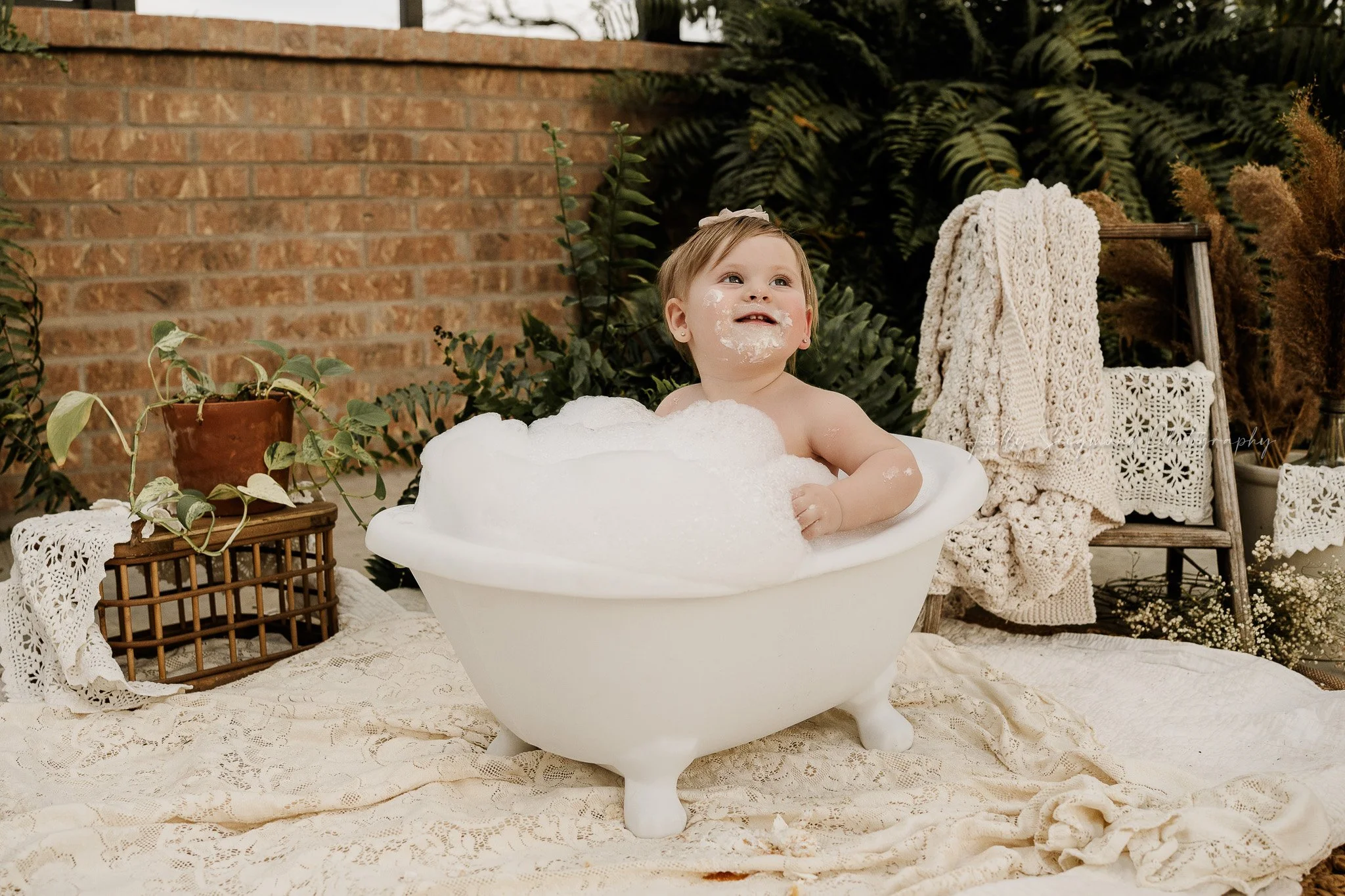 First birthday photo session with baby girl in a clawfoot bathtub cleaning up after a smash cake session in Central Texas