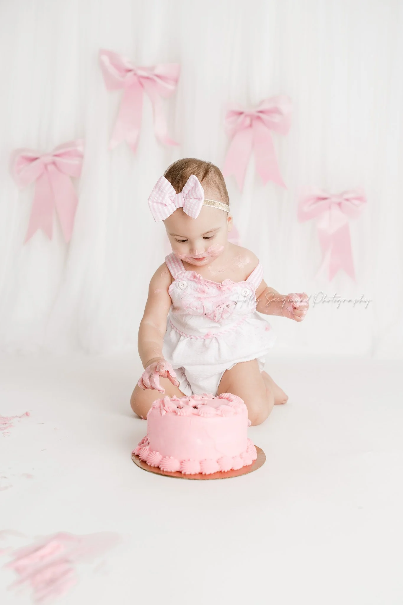 Little girls first birthday smash cake session with pink bows in a flash photography studio near Elgin, Texas