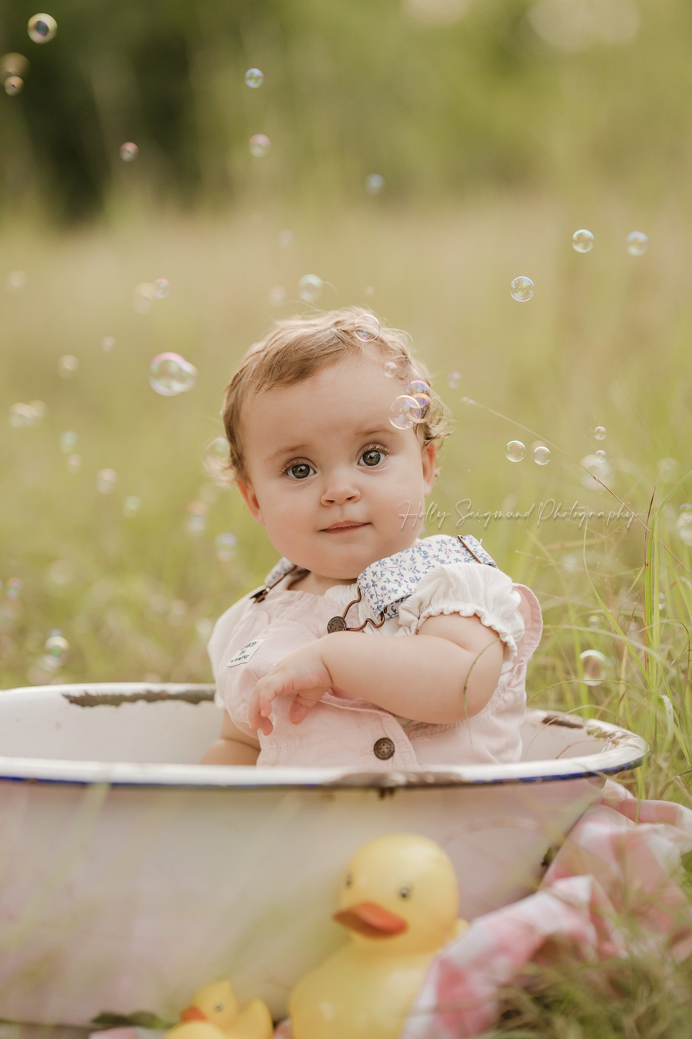 Girls first birthday photos in the spring grass in a white metal tub with rubber ducks and bubbles, outdoors in Lexington, Texas