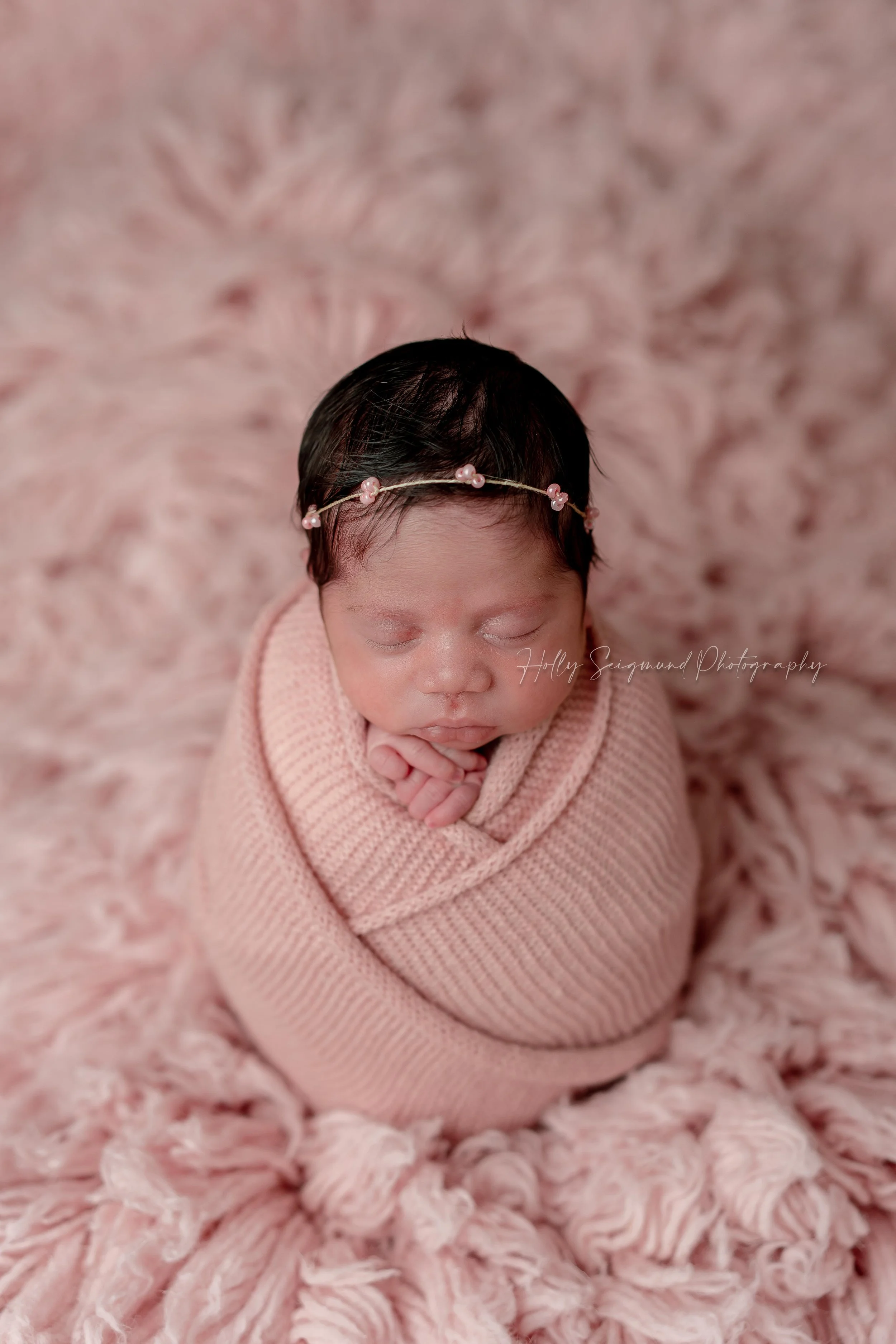 Baby newborn girl wrapped in pink on a fluffy backdrop during a studio newborn session in Lexington, Texas