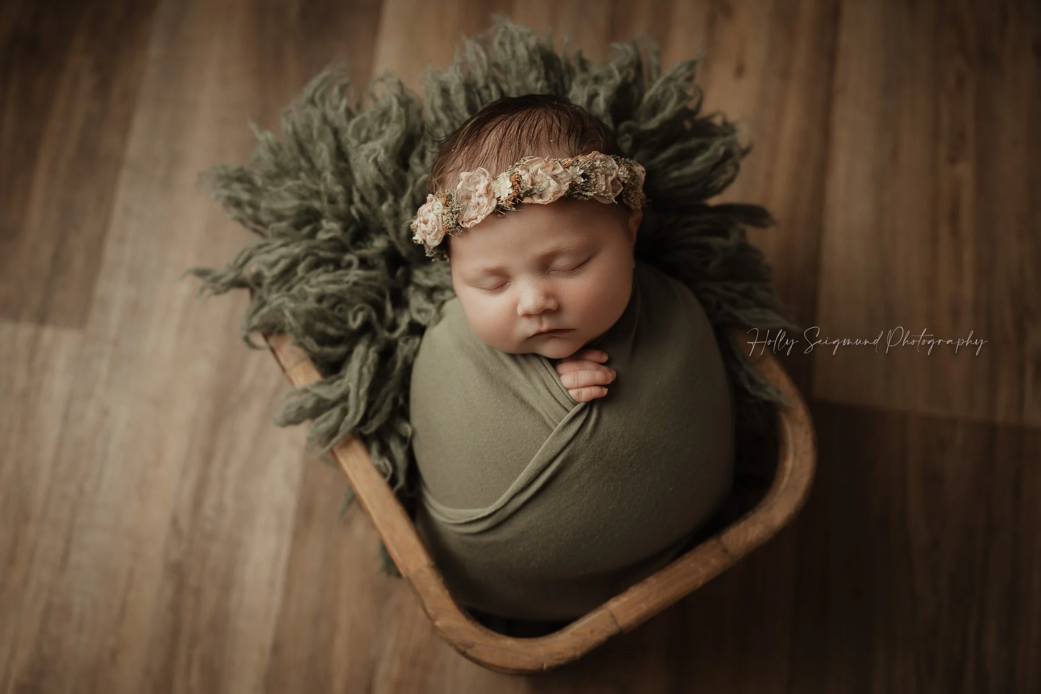 Newborn baby girl in a wooden basket with a floral crown on a wooden floor in a Central Texas newborn photography studio