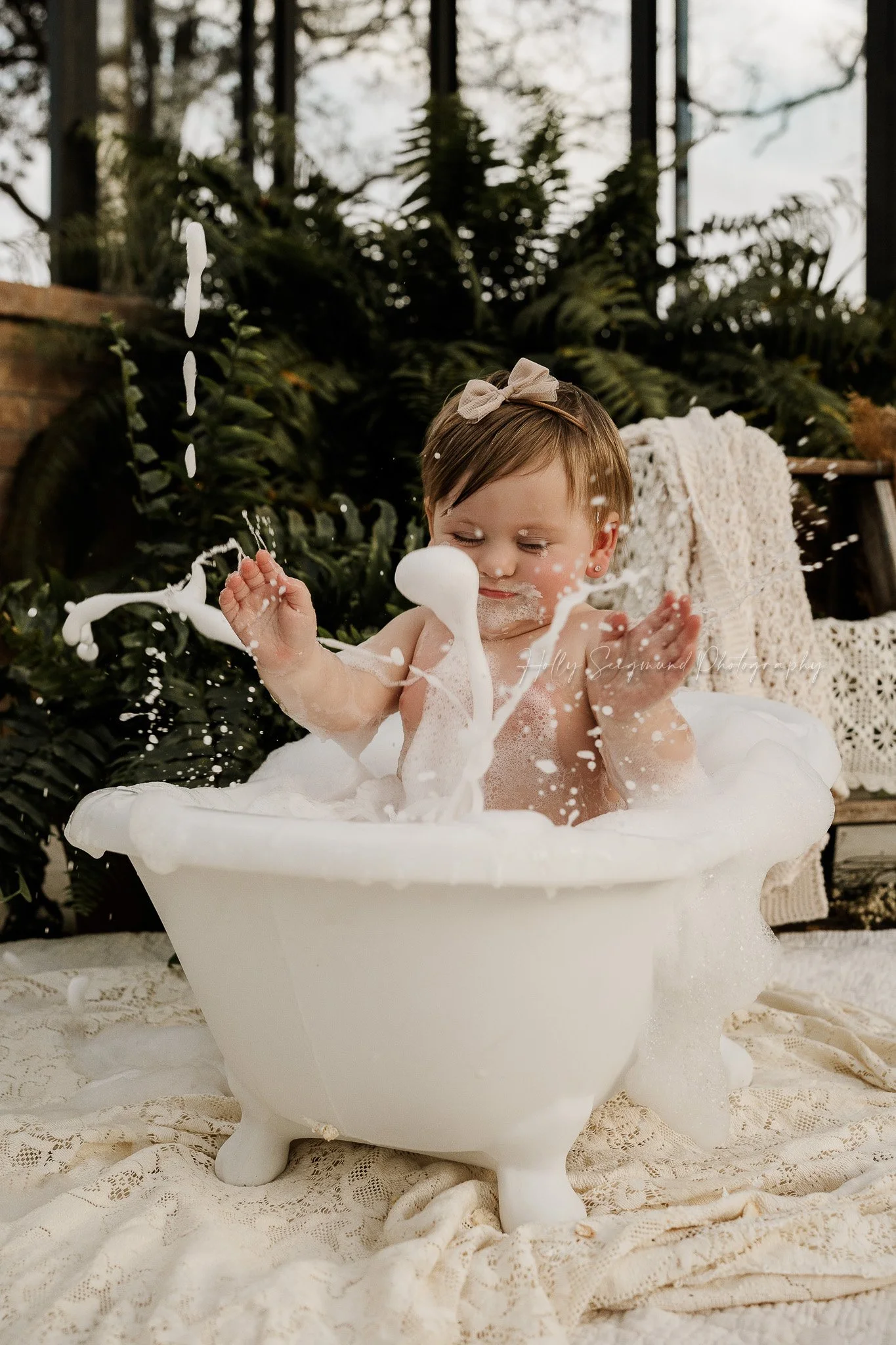First birthday photo session with baby girl splashing bubbles in a clawfoot bathtub cleaning up after a smash cake session in Central Texas