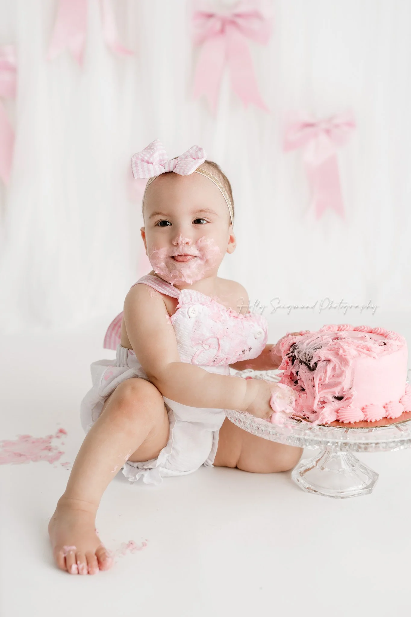 Little girls first birthday smash cake session with pink bows in a flash photography studio near Austin, Texas