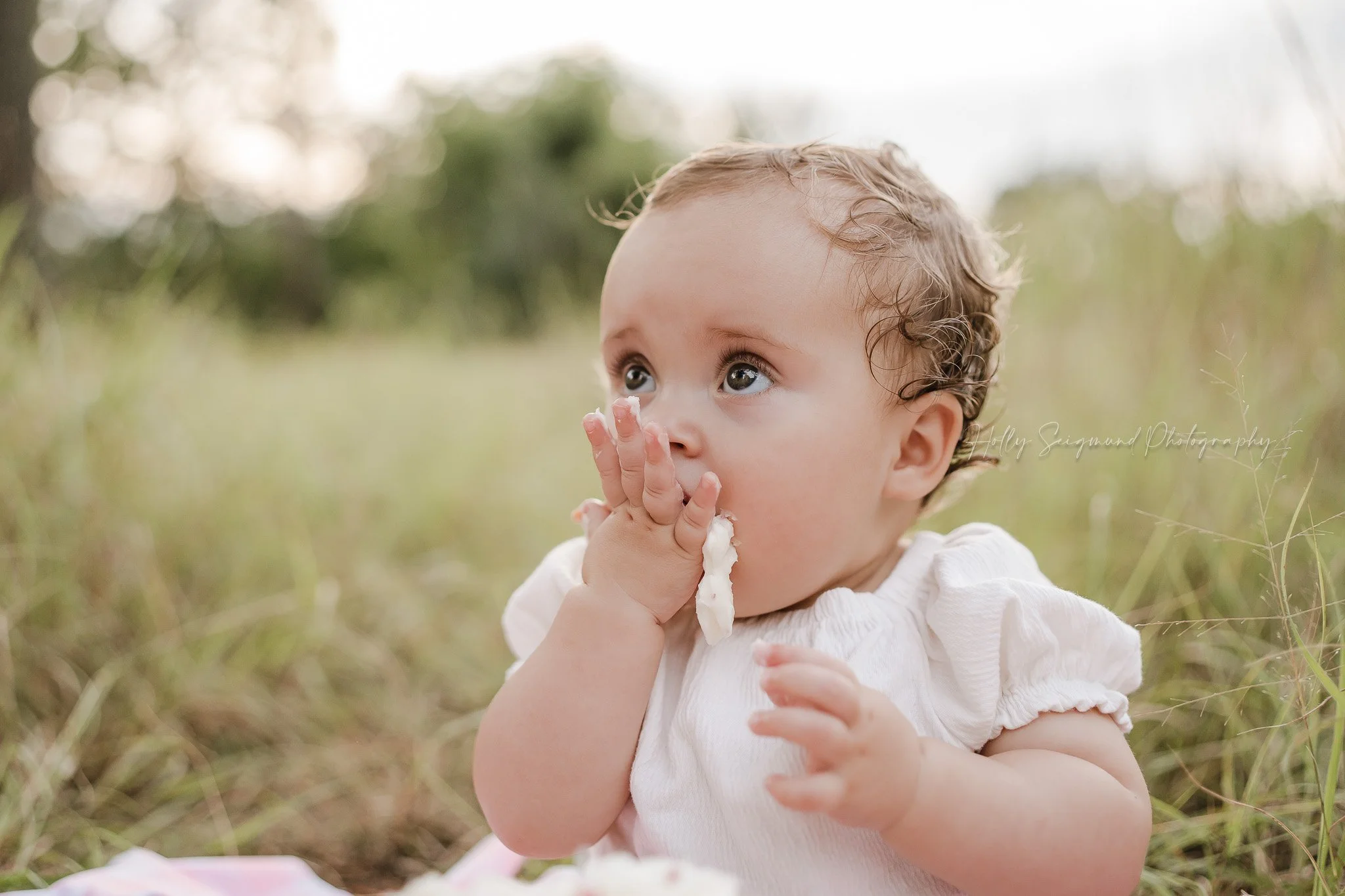 Little girl eating cake on her first birthday session in the grass near Lexington, Texas