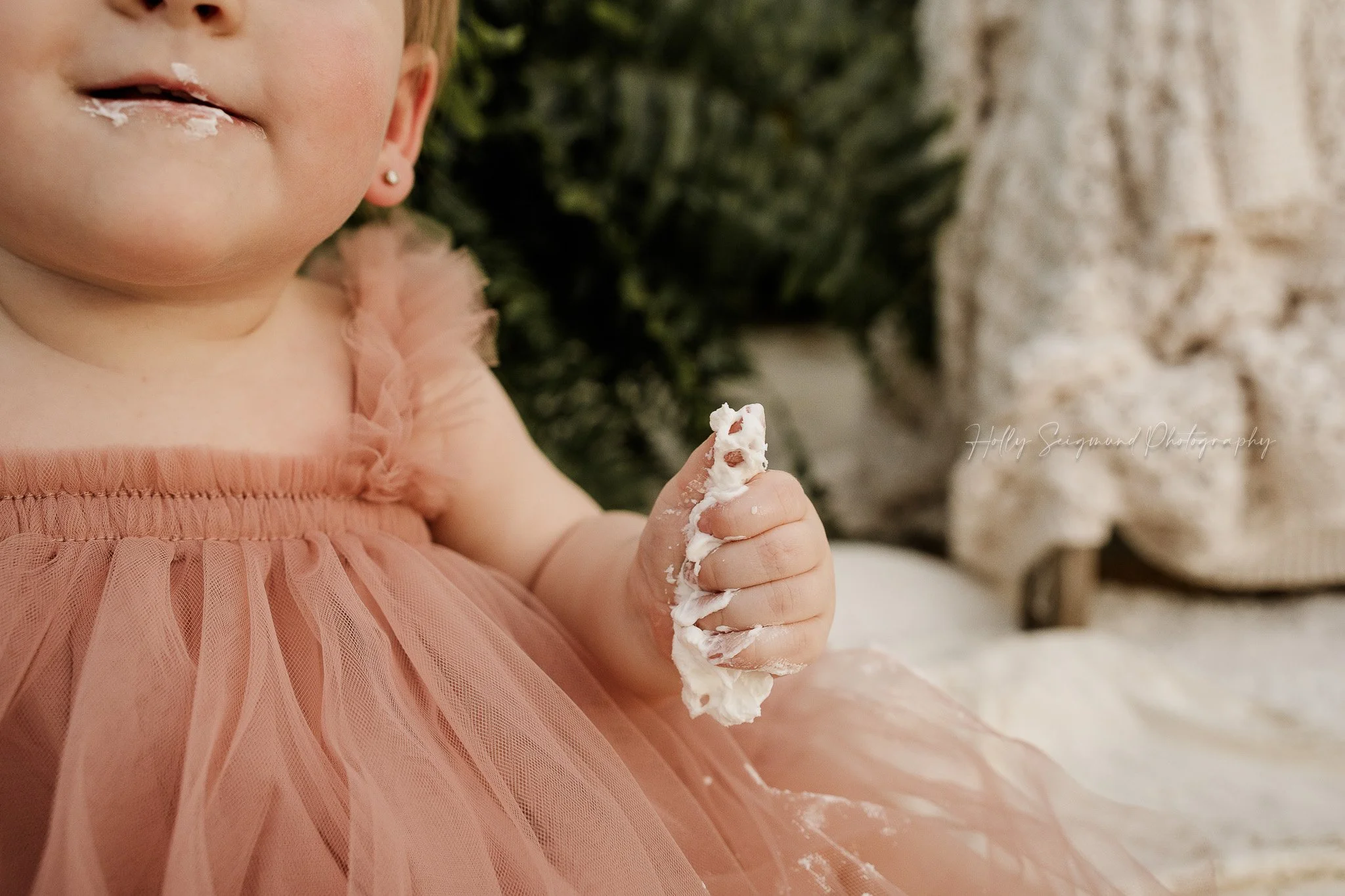 Boho style smash cake session with baby girls hand full of icing in greenhouse in Lee County Texas