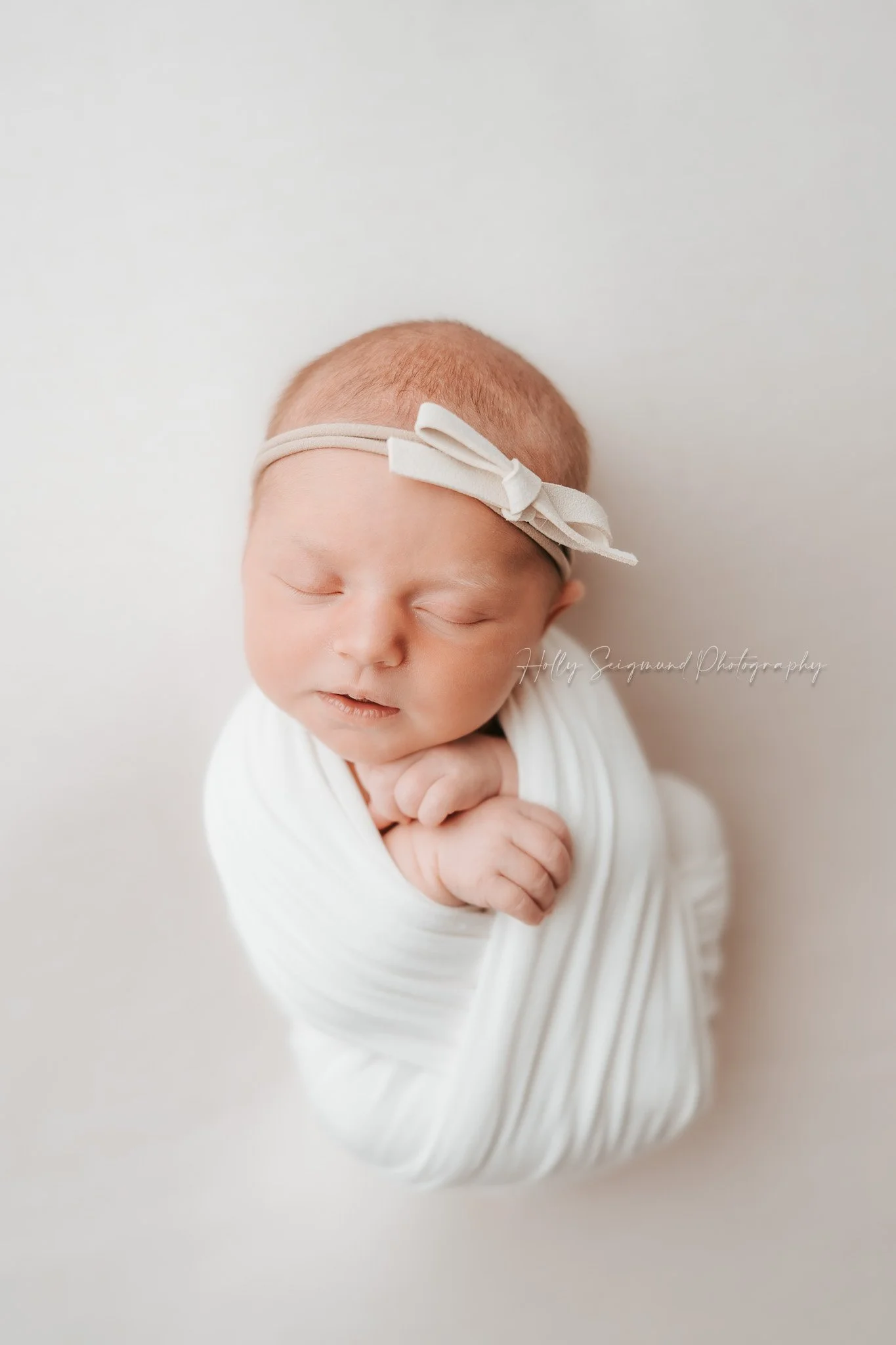 Newborn girl wrapped in white with bow at photography studio in Lee County